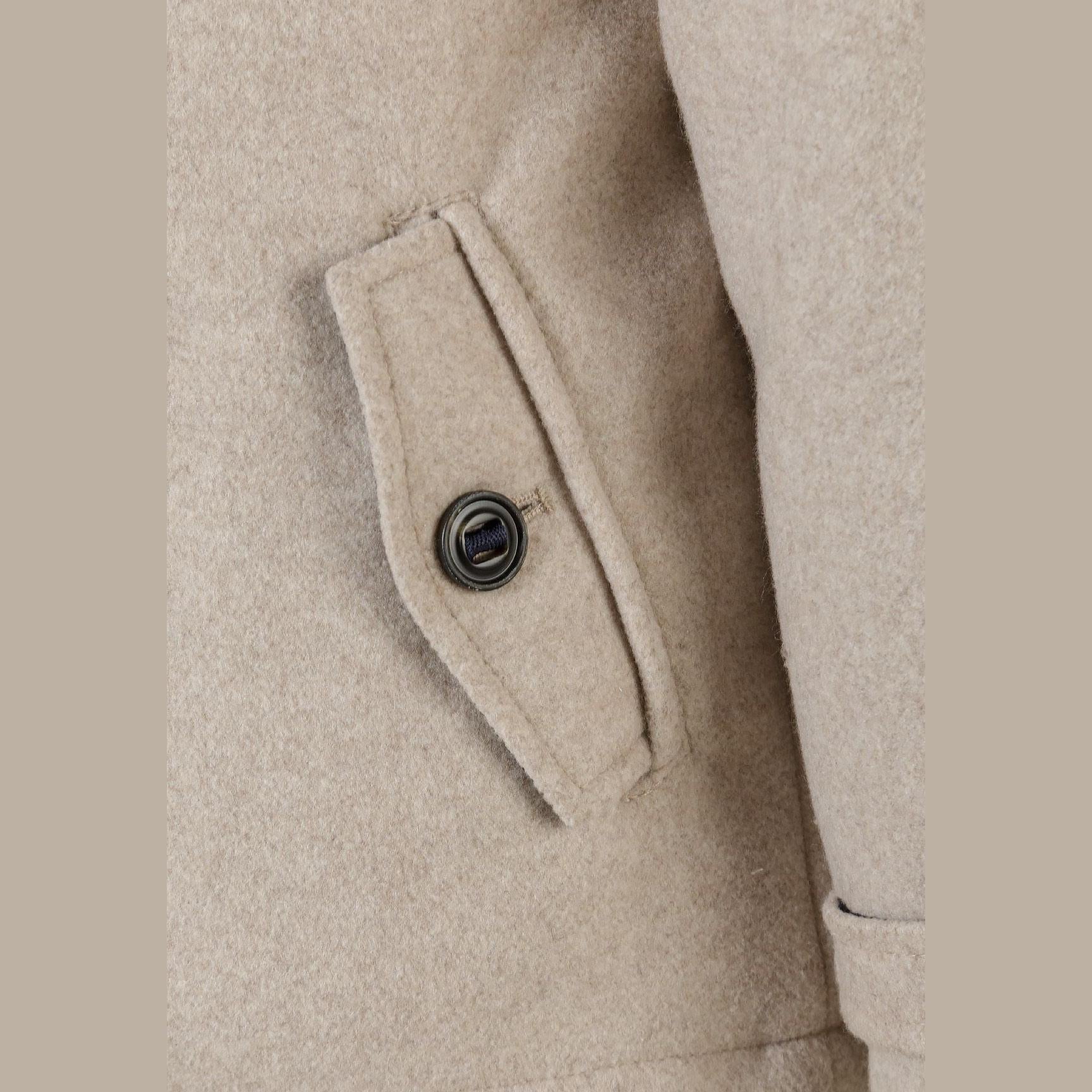 Close-up detail of coat sleeve showing buttoned cuff tab with dark button on beige wool-blend fabric