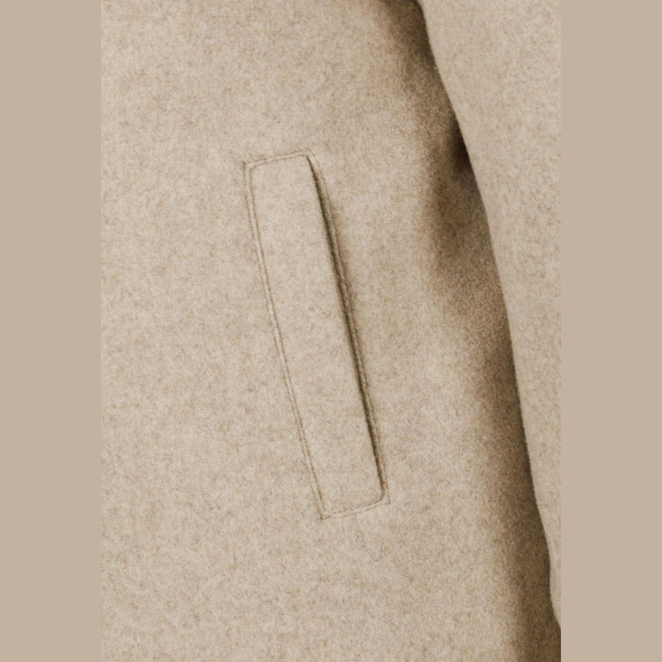 Close-up detail of beige coat showing side pocket construction and fabric texture