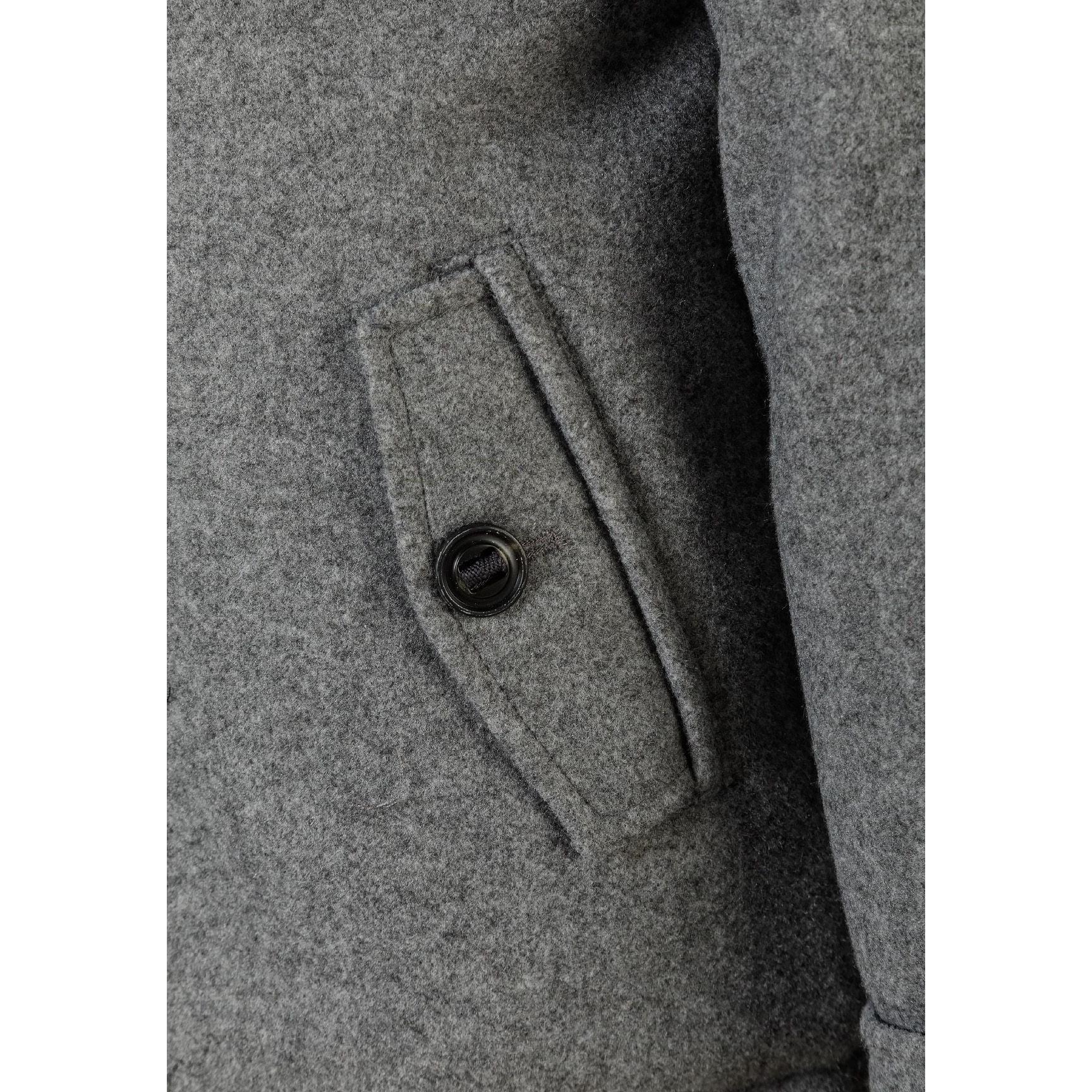 Close-up detail of grey coat showing front pocket with button closure and fabric texture of the wool-blend material