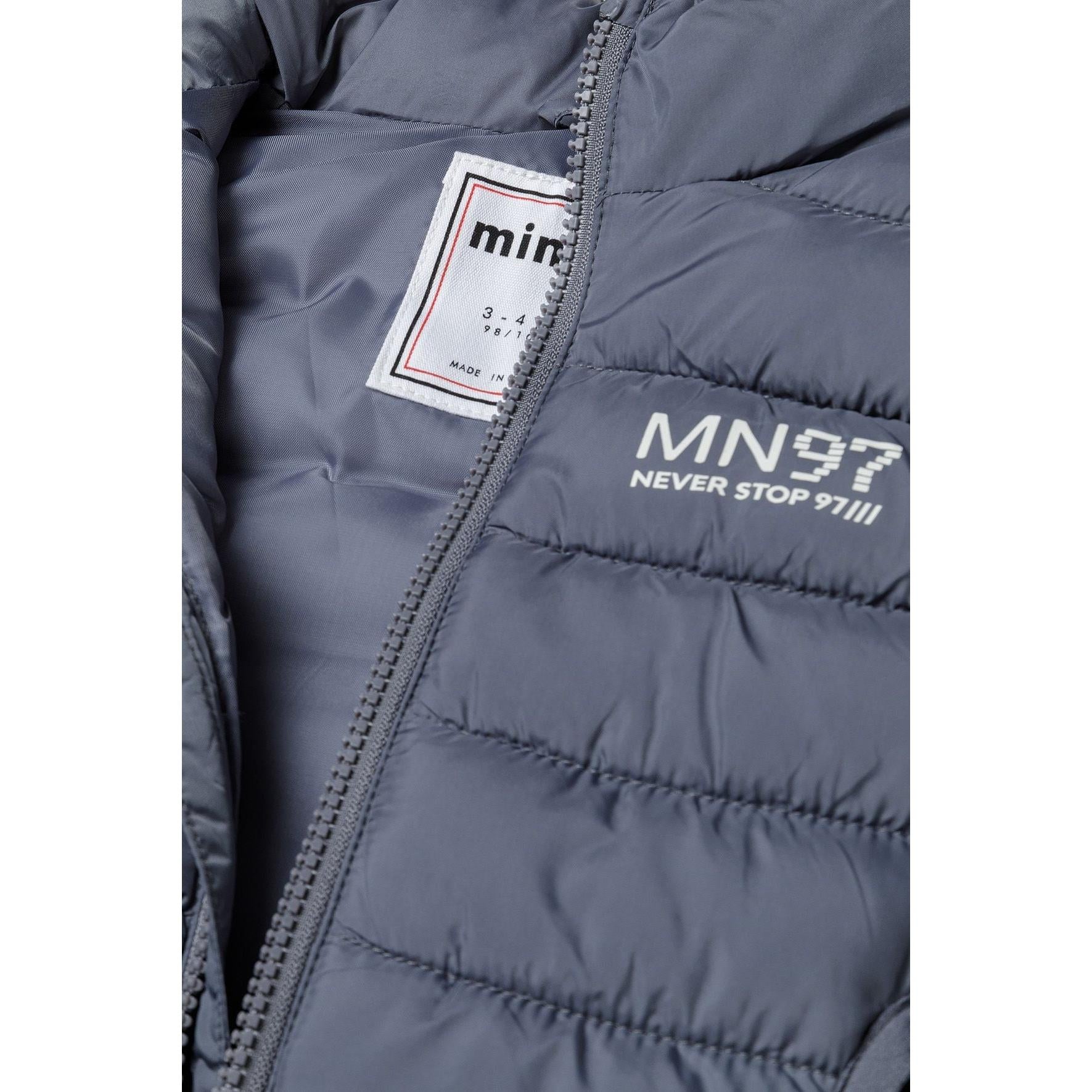 Close-up detail of grey padded gilet showing MN97 chest print, Minoti internal label and quilted texture