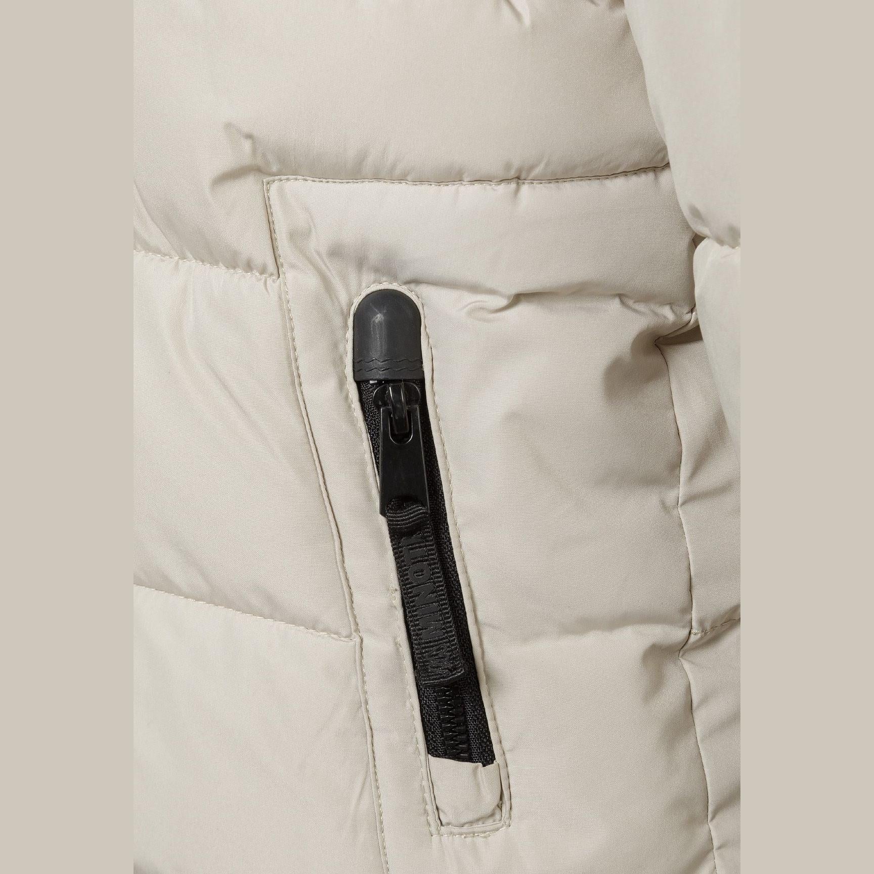 Close-up detail of cream padded jacket showing black branded patch with mountain logo and Minoti text on sleeve