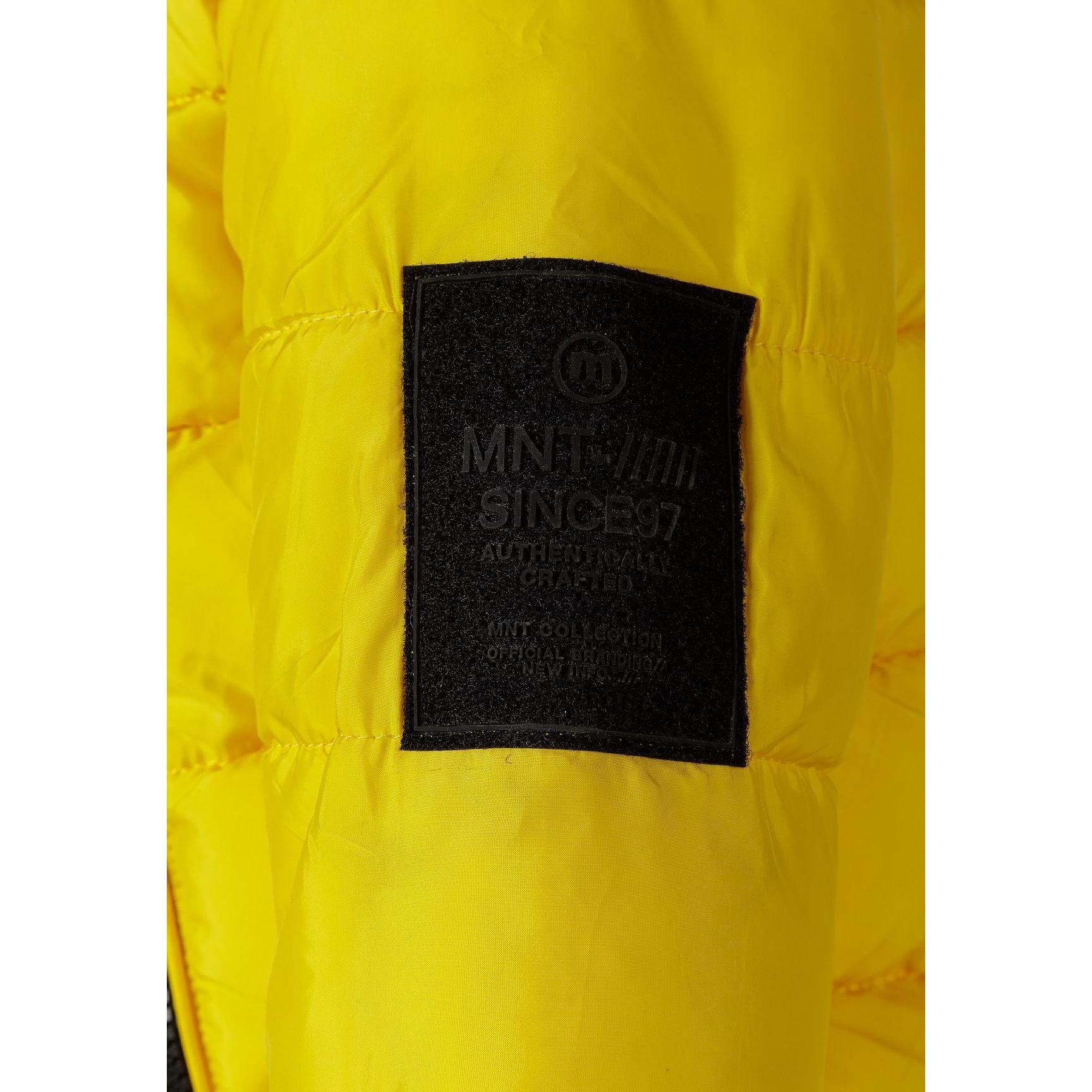 Close-up detail of black fabric label on yellow padded jacket showing Minoti brand text and sizing information