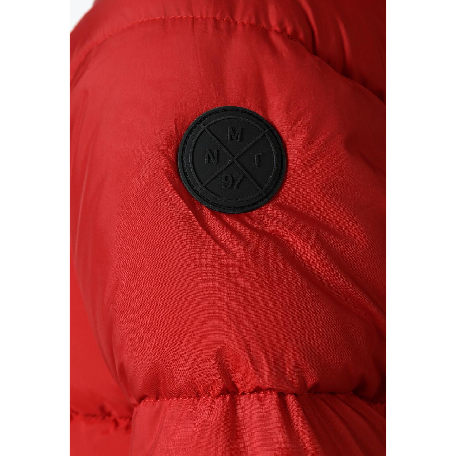 Close-up detail of black circular Minoti badge with crossed design and brand lettering on red padded jacket sleeve