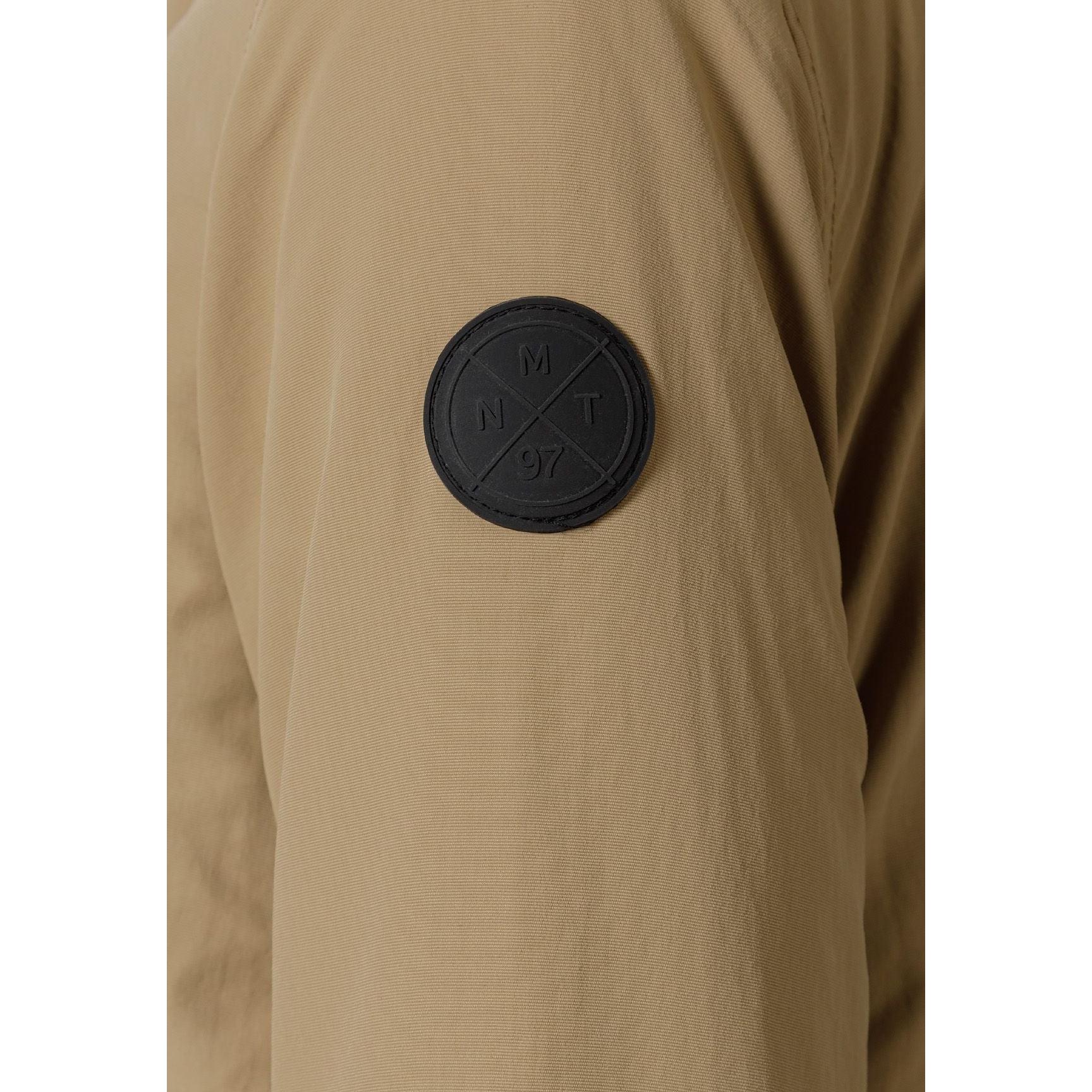 Close-up detail of black circular logo patch on beige parka jacket sleeve showing crossed design elements