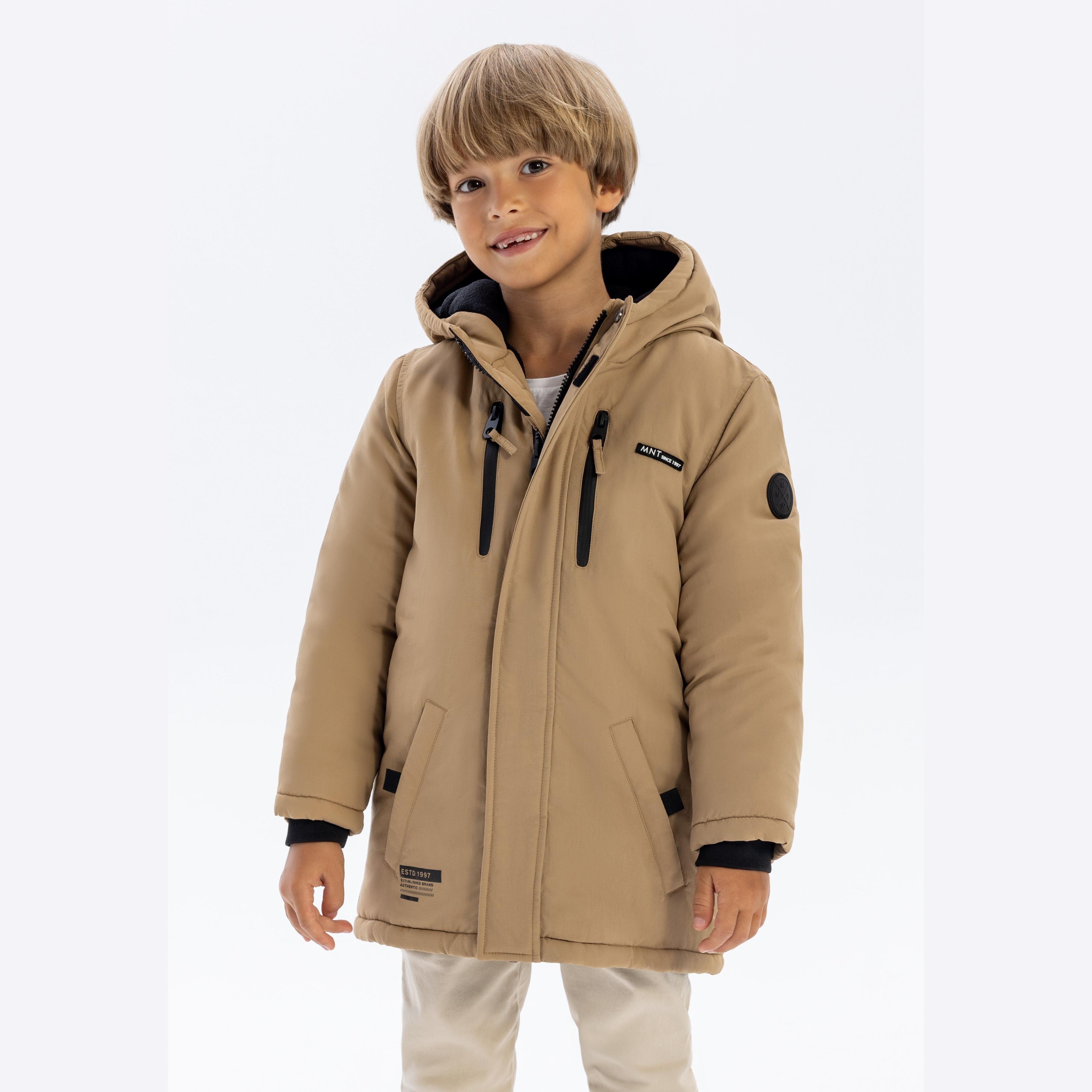 Young boy wearing beige parka jacket with hood up, smiling at camera against white background