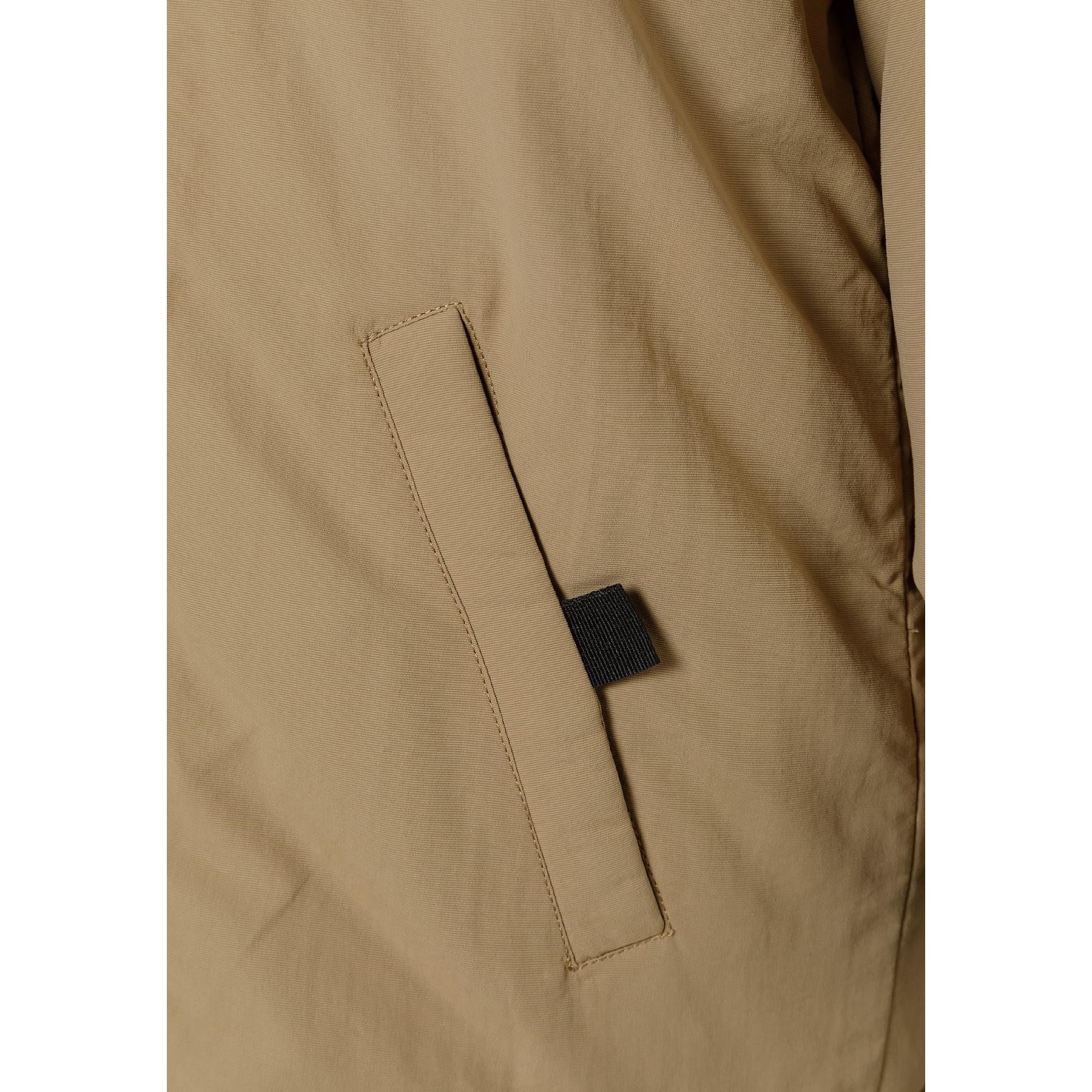 Close-up detail of black circular logo patch on beige parka jacket sleeve showing crossed design elements