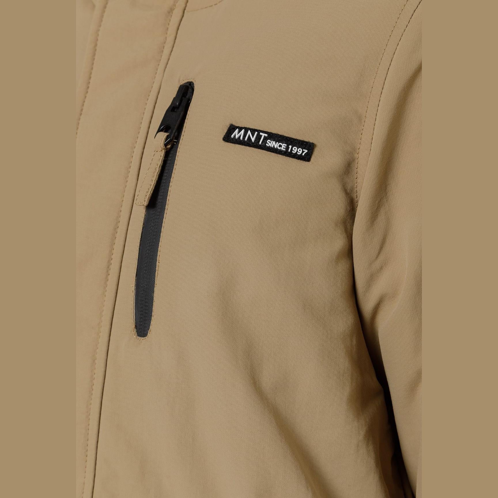 Close-up detail of black circular logo patch on beige parka jacket sleeve showing crossed design elements
