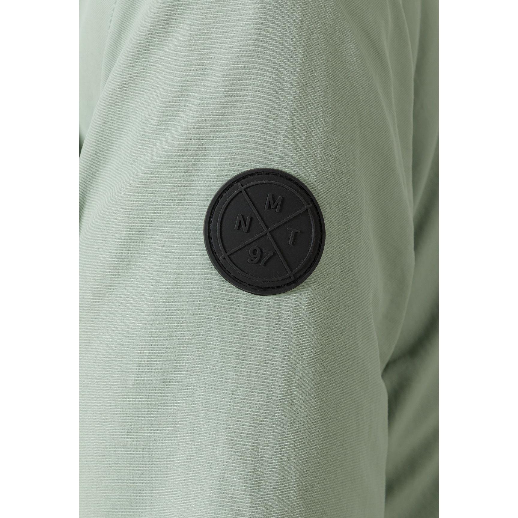 Close-up detail of black circular badge with crossed design on sage green fabric of parka jacket