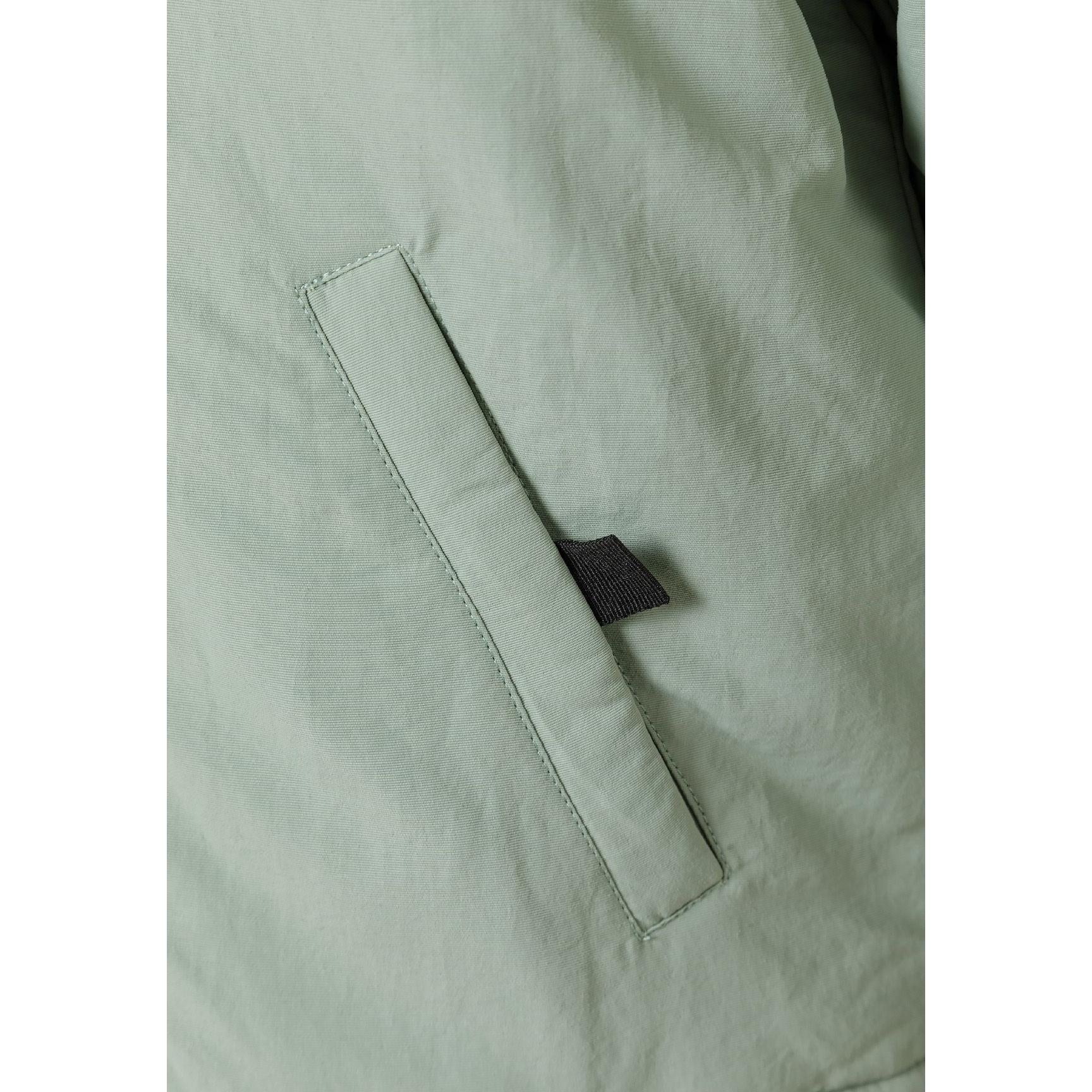 Close-up detail of black circular badge with crossed design on sage green fabric of parka jacket