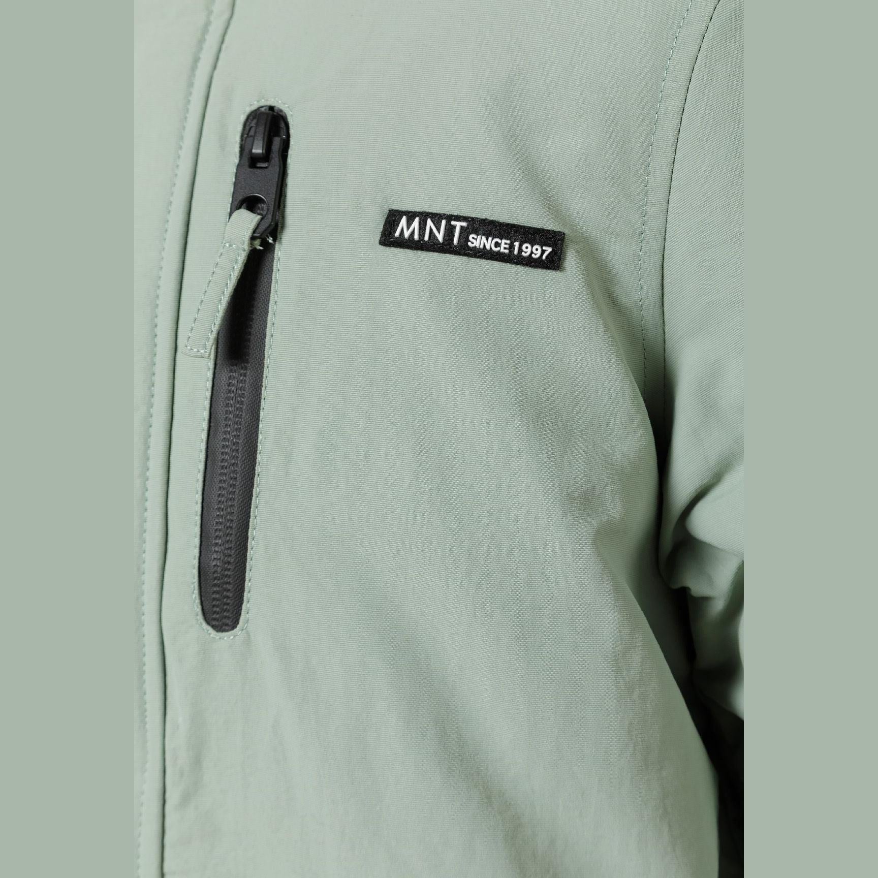 Close-up detail of black circular badge with crossed design on sage green fabric of parka jacket