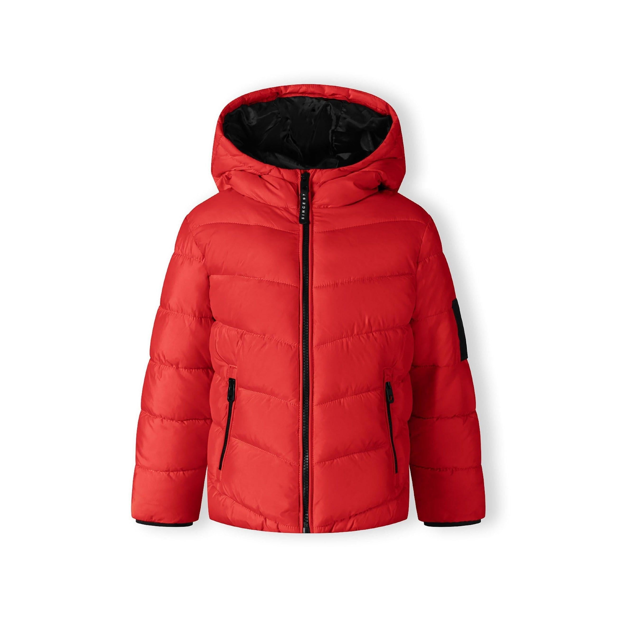 Close-up detail of black Minoti brand patch on red quilted jacket fabric showing logo and text