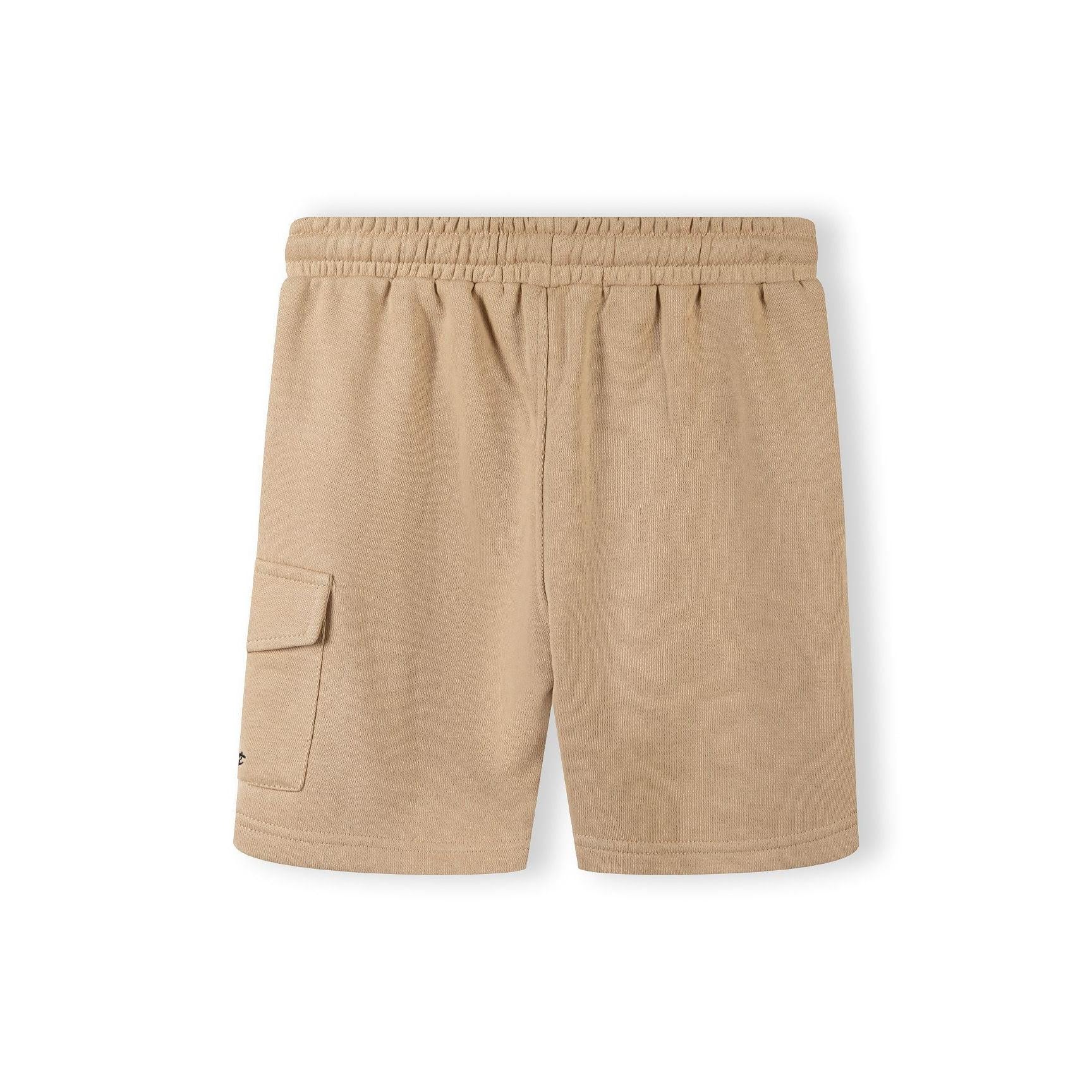 Close-up detail of beige cotton shorts showing elasticated waistband with black drawstring and Minoti label