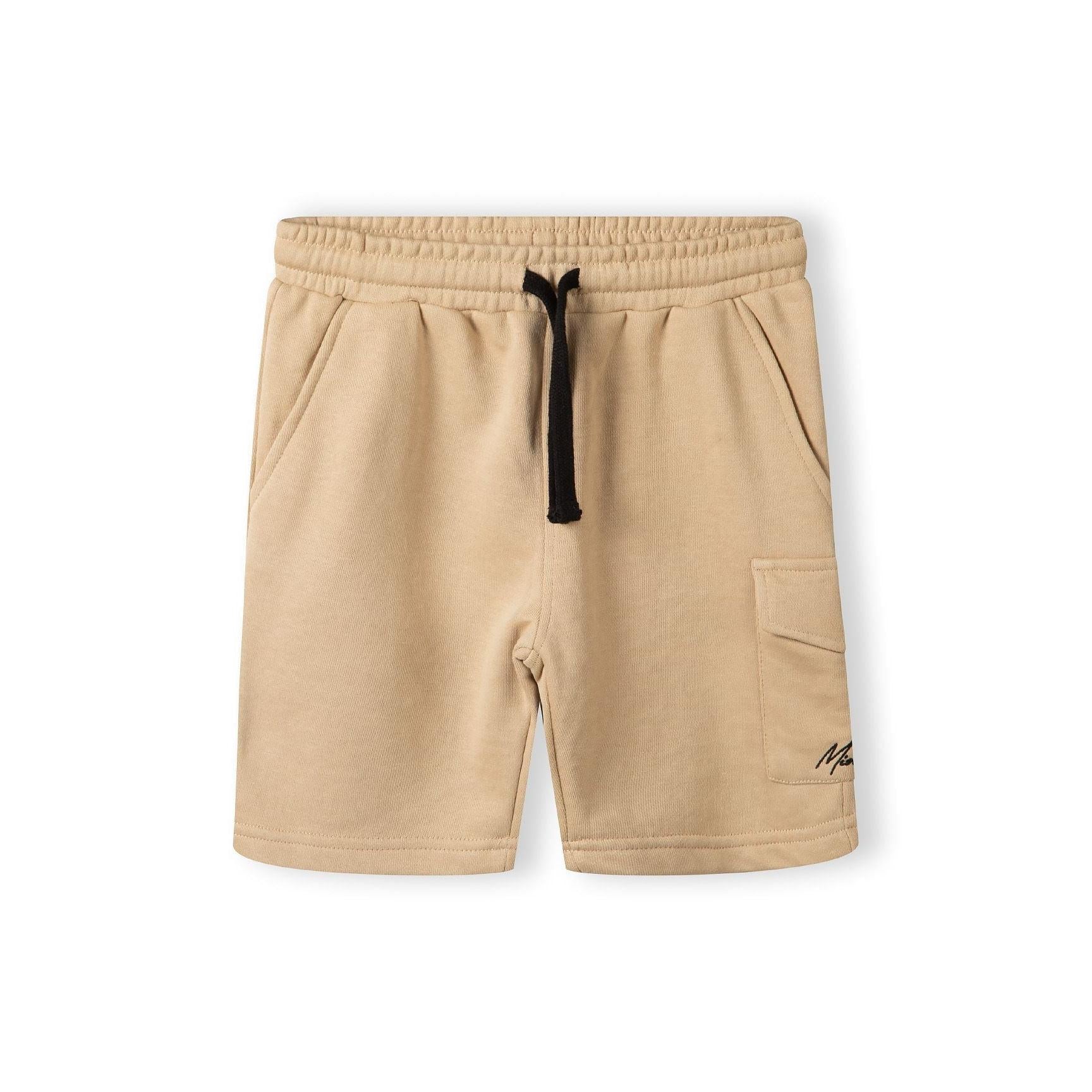 Close-up detail of beige cotton shorts showing elasticated waistband with black drawstring and Minoti label