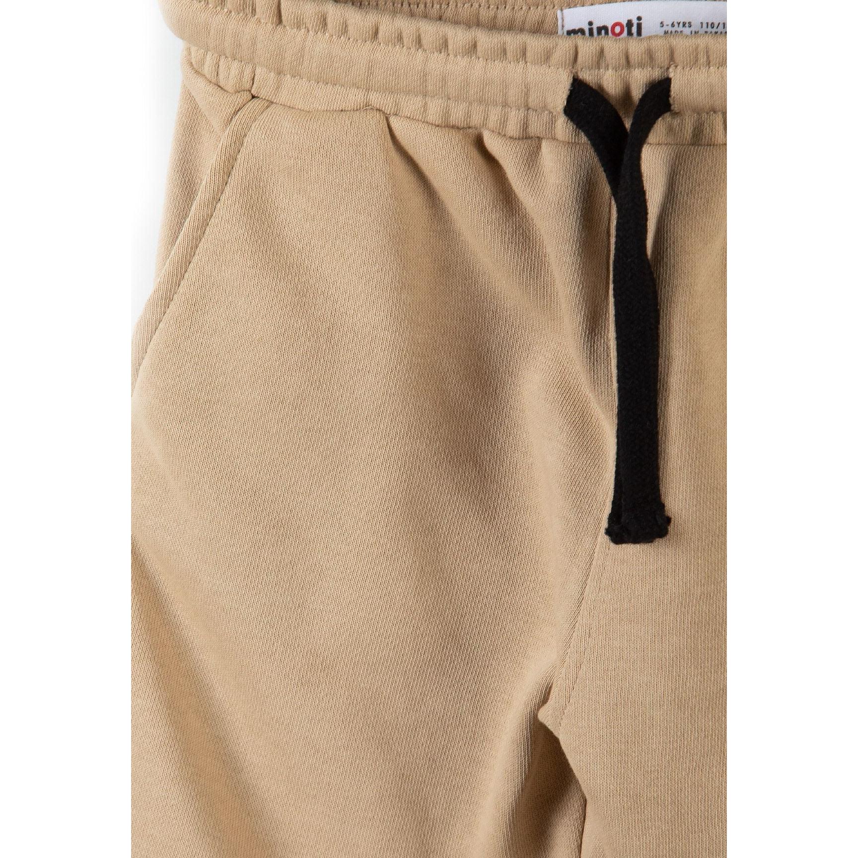 Close-up detail of beige cotton shorts showing elasticated waistband with black drawstring and Minoti label