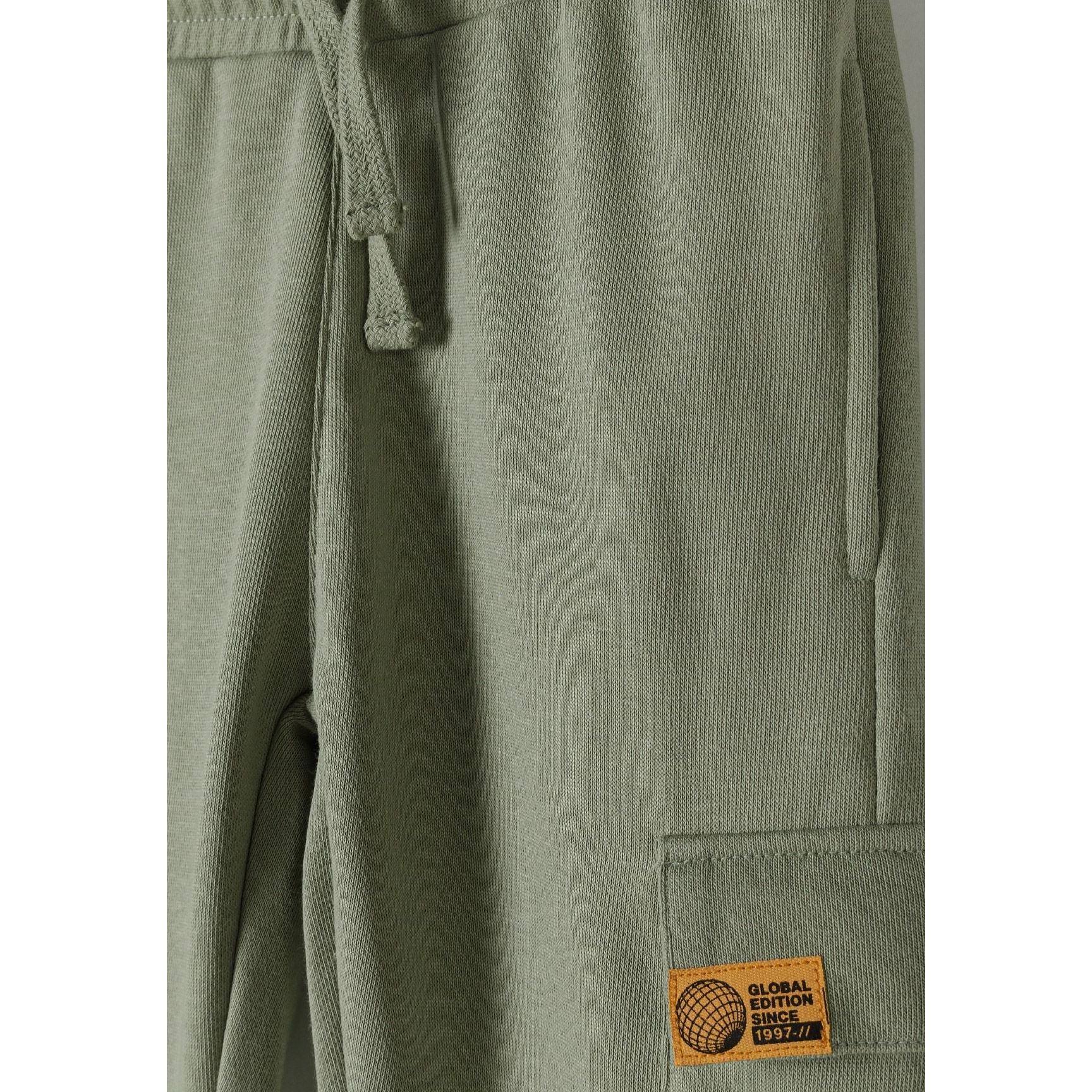 Close-up of olive green fleece joggers showing drawstring waist detail and orange logo patch on leg