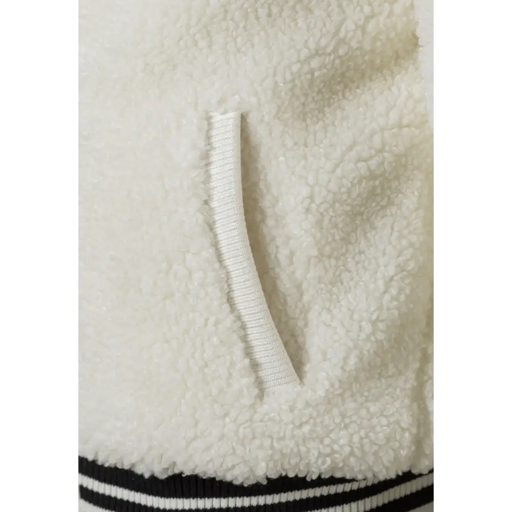 Close-up detail of cream borg fabric texture showing side pocket with ribbed hem trim in navy and white stripes