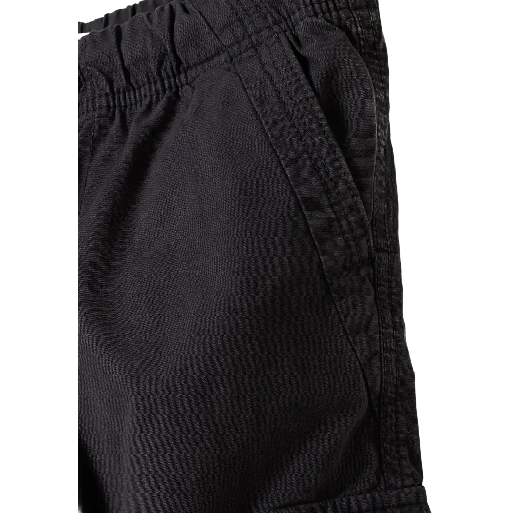 Close-up detail of black cargo trousers showing elasticated waistband texture, side seam construction and pocket detail against black background
