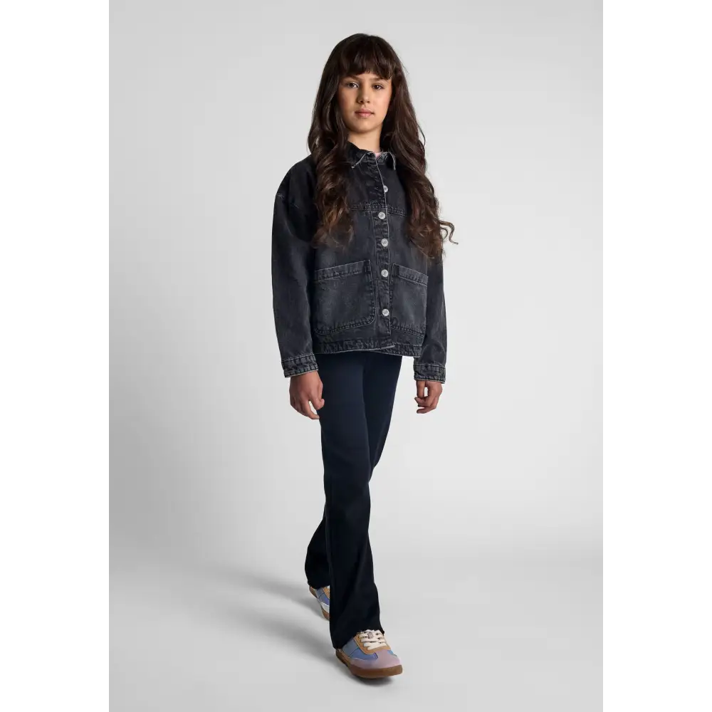 Full length view of girl in oversized black acid wash denim jacket with dark jeans and sneakers on white studio background