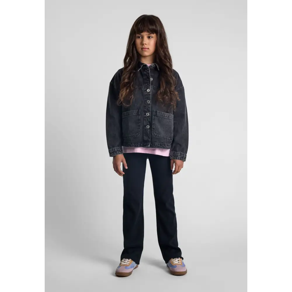 Girl wearing oversized black acid wash denim jacket with pink top and dark jeans, standing on white background