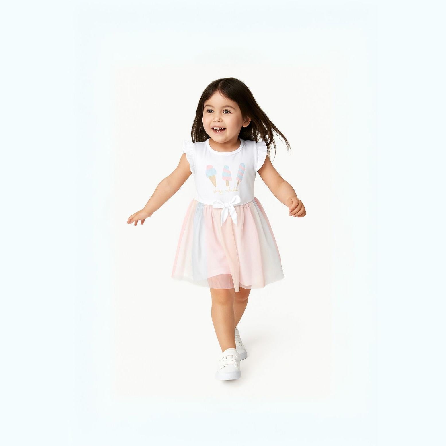 Young girl with dark hair running in white dress with flutter sleeves and rainbow tulle skirt, smiling on white background