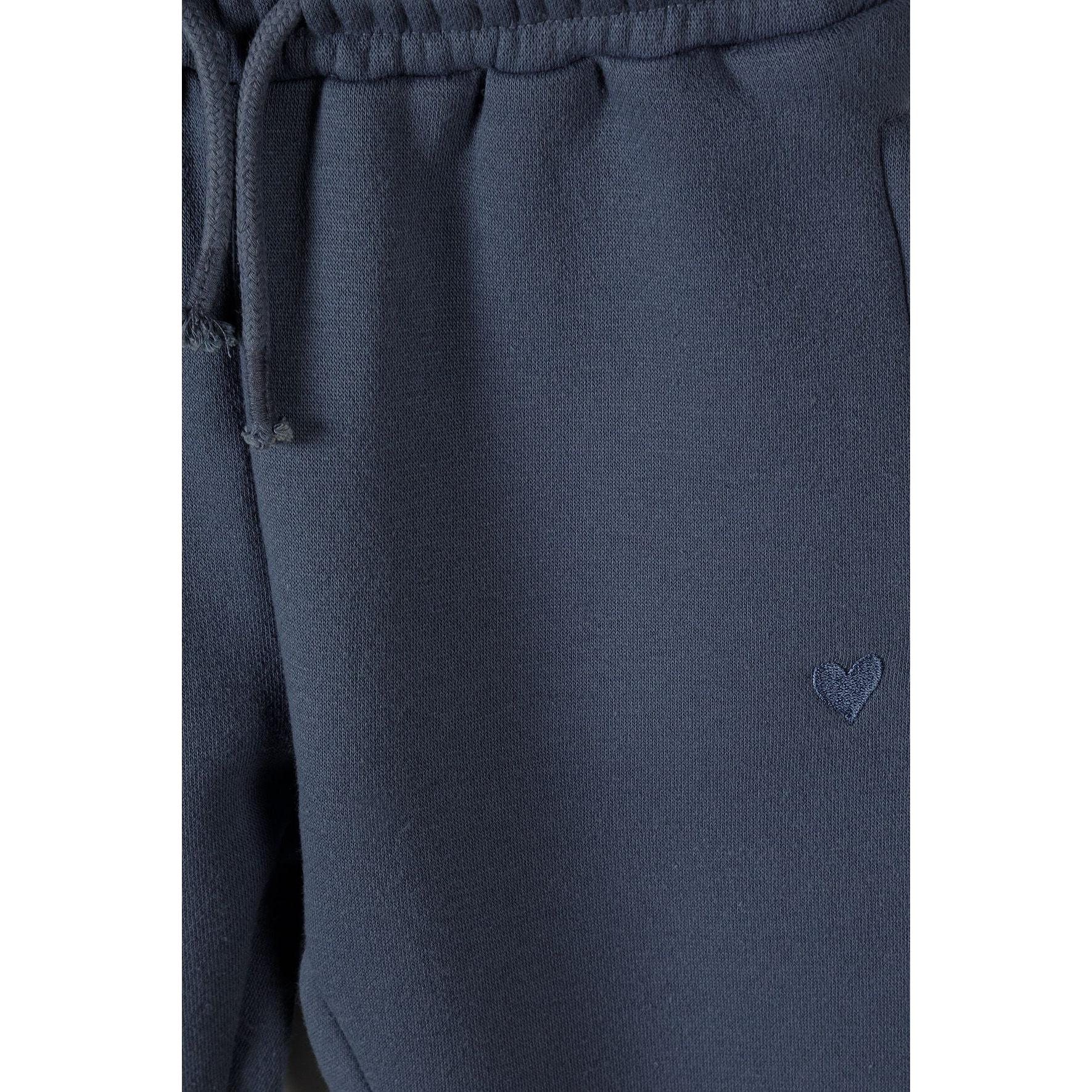 Close-up detail of blue fleece joggers showing elasticated waistband with drawstring and subtle heart embroidery on leg
