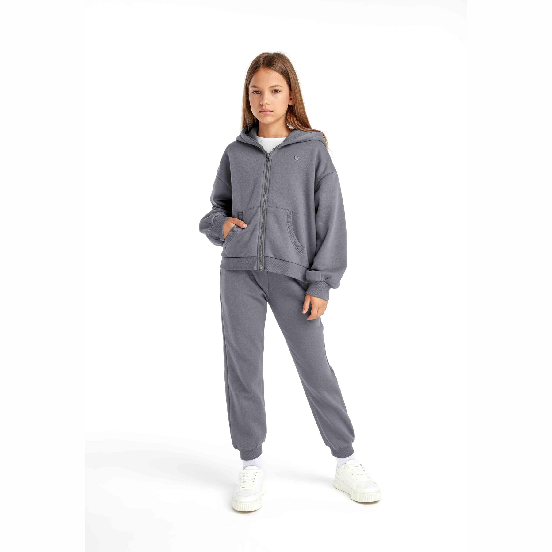 Girl wearing grey fleece hoodie and matching joggers in full length studio shot against white background