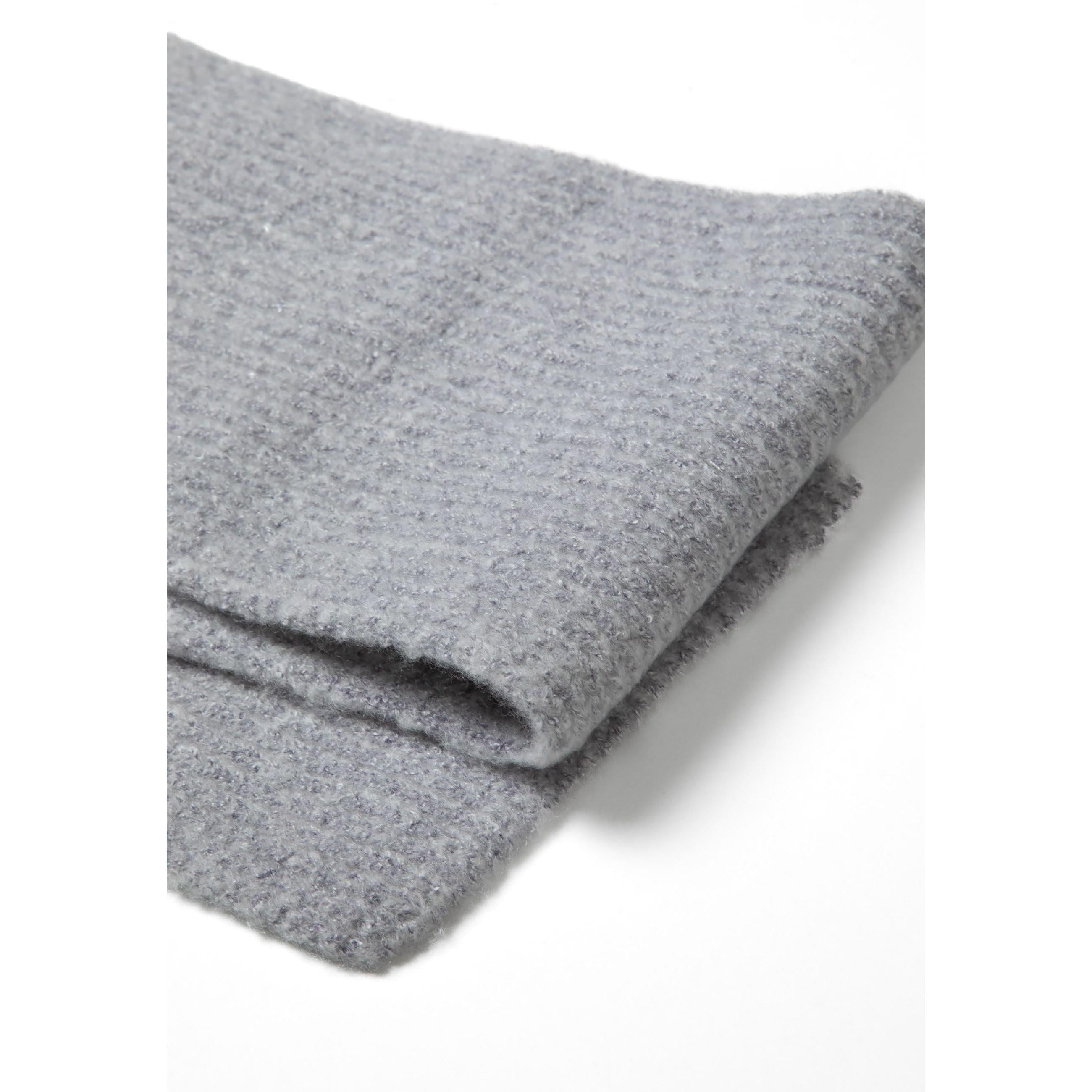 Close-up detail of grey ribbed knit fabric texture showing small black metal badge with brand logo