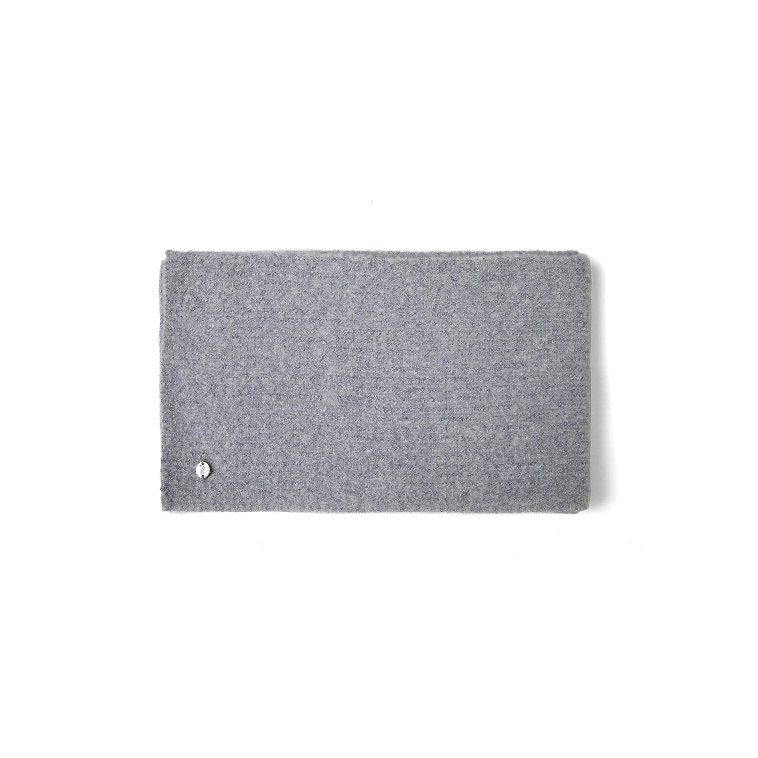 Close-up detail of grey ribbed knit fabric texture showing small black metal badge with brand logo
