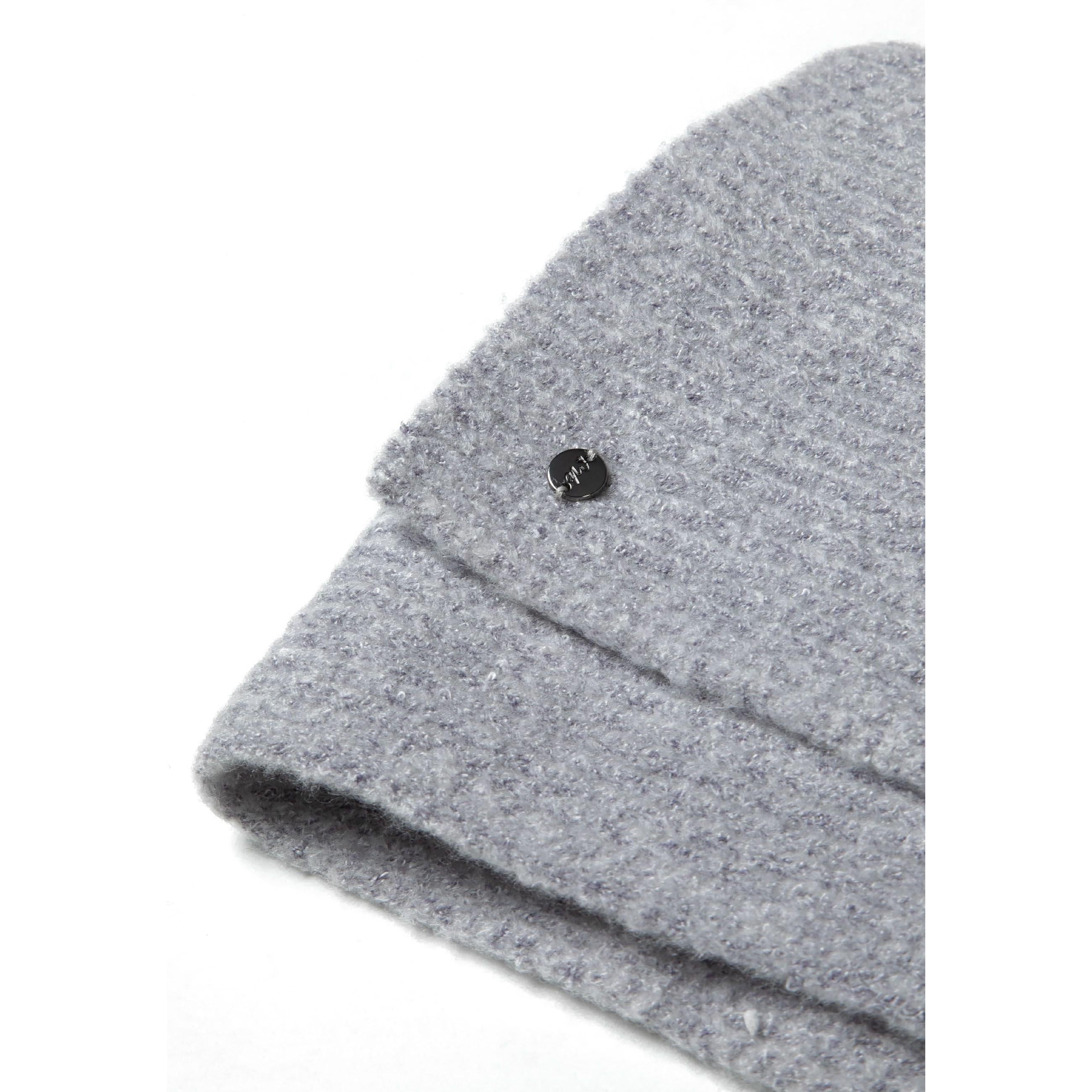 Close-up detail of grey ribbed knit fabric texture showing small black metal badge with brand logo