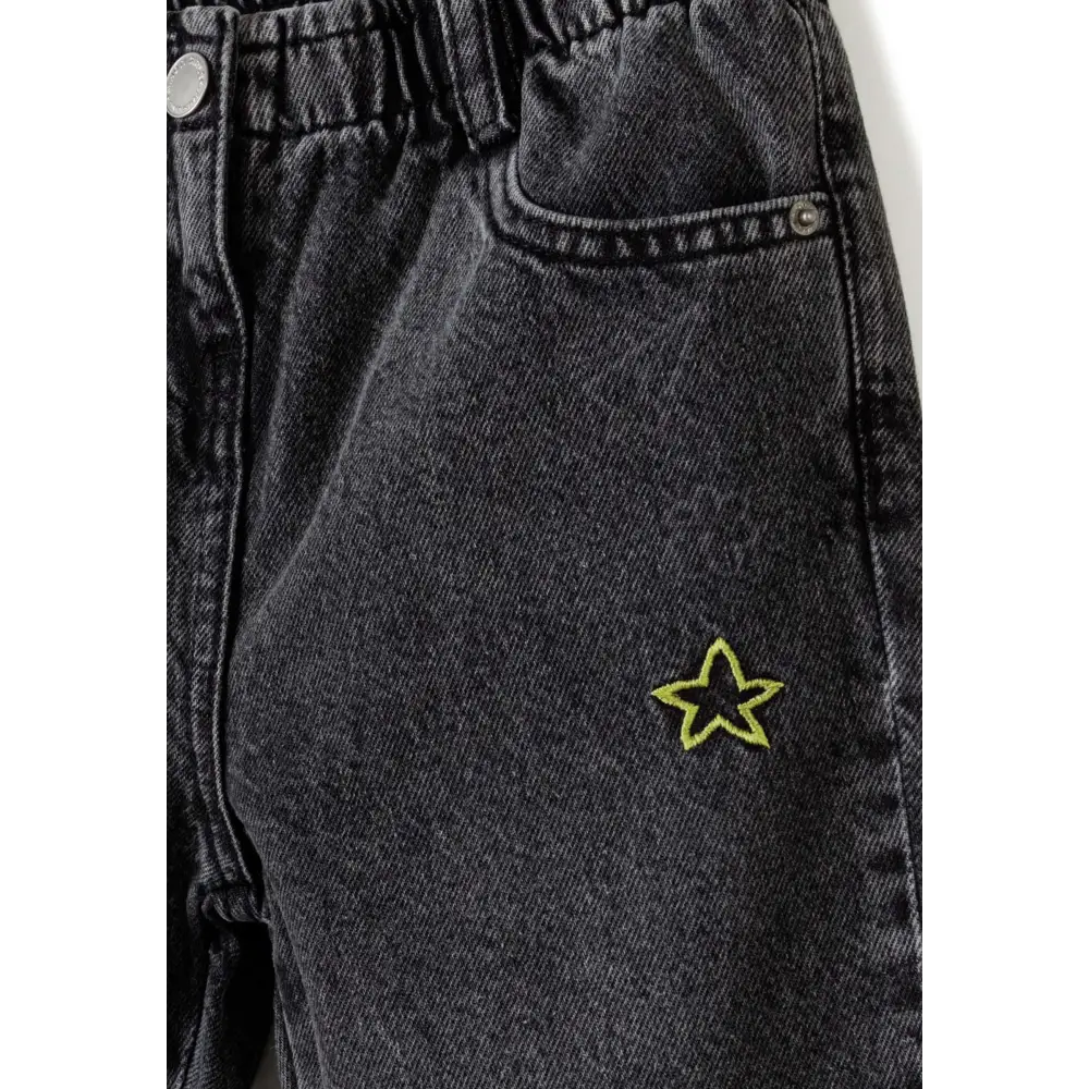 Close-up detail of black denim jeans showing yellow star embroidery on front pocket and elasticated waistband construction