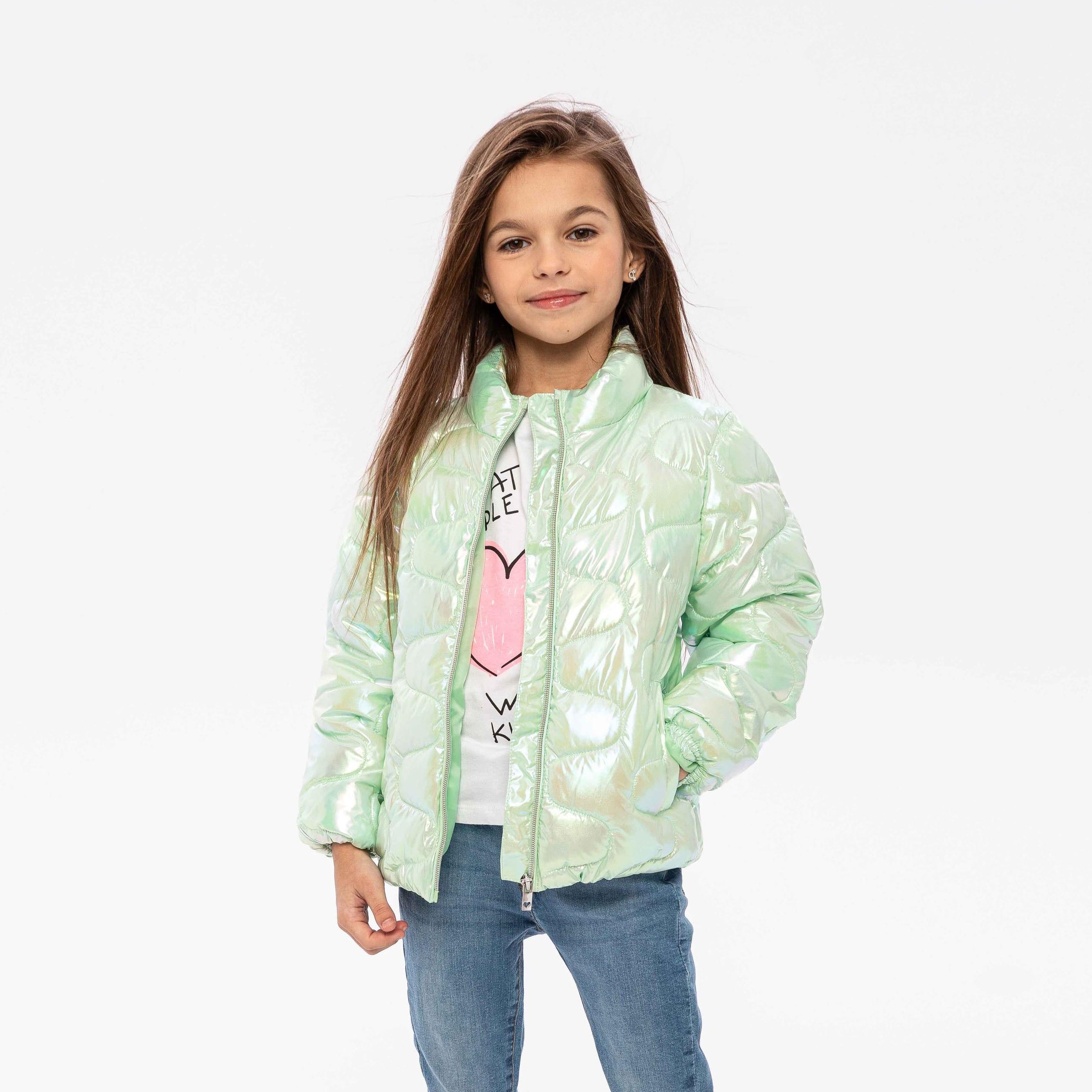 Girl wearing mint green iridescent quilted jacket over white top and jeans, standing against white background