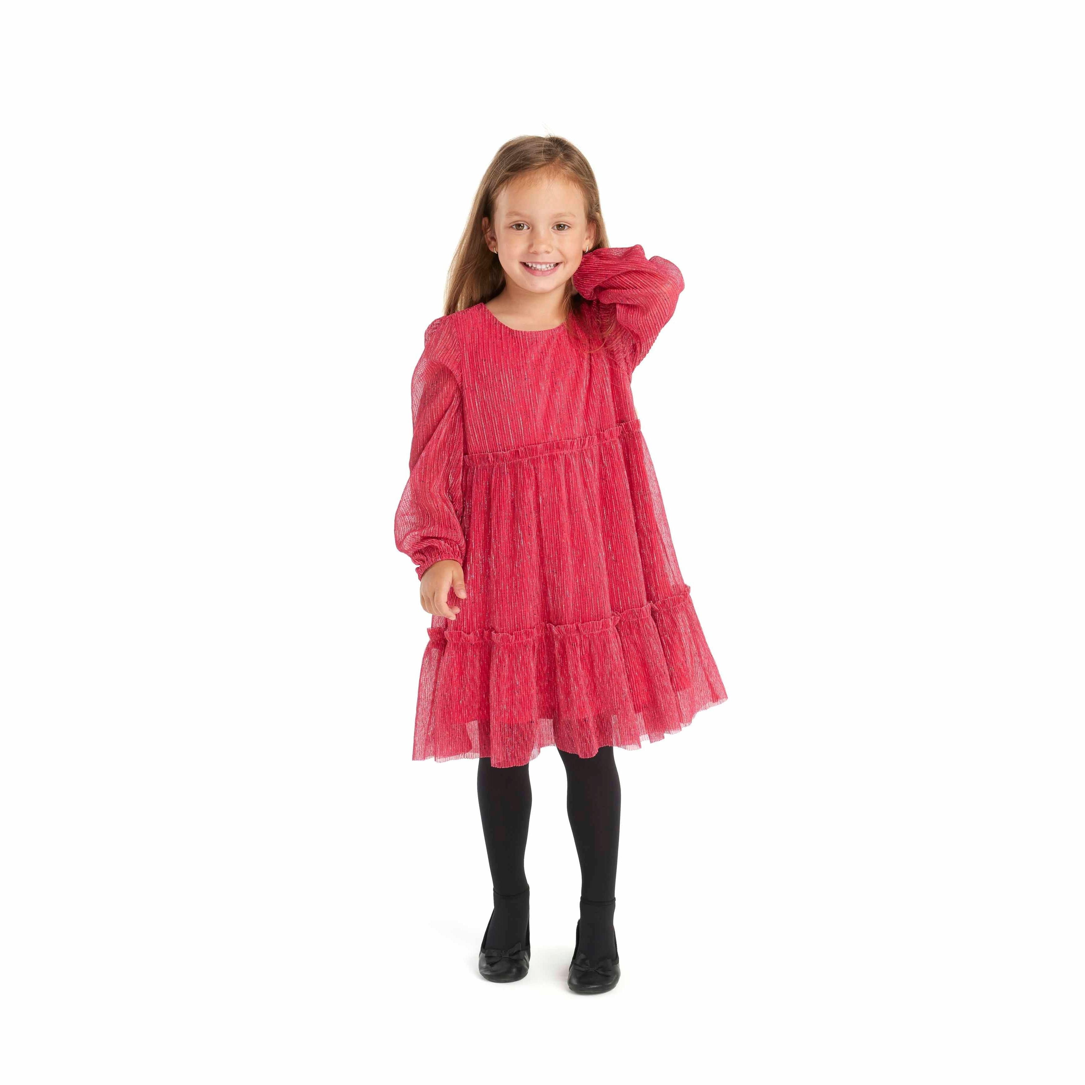 Young girl wearing pink sparkle pleated party dress with long balloon sleeves and tiered skirt, paired with black tights and shoes, posing on white background