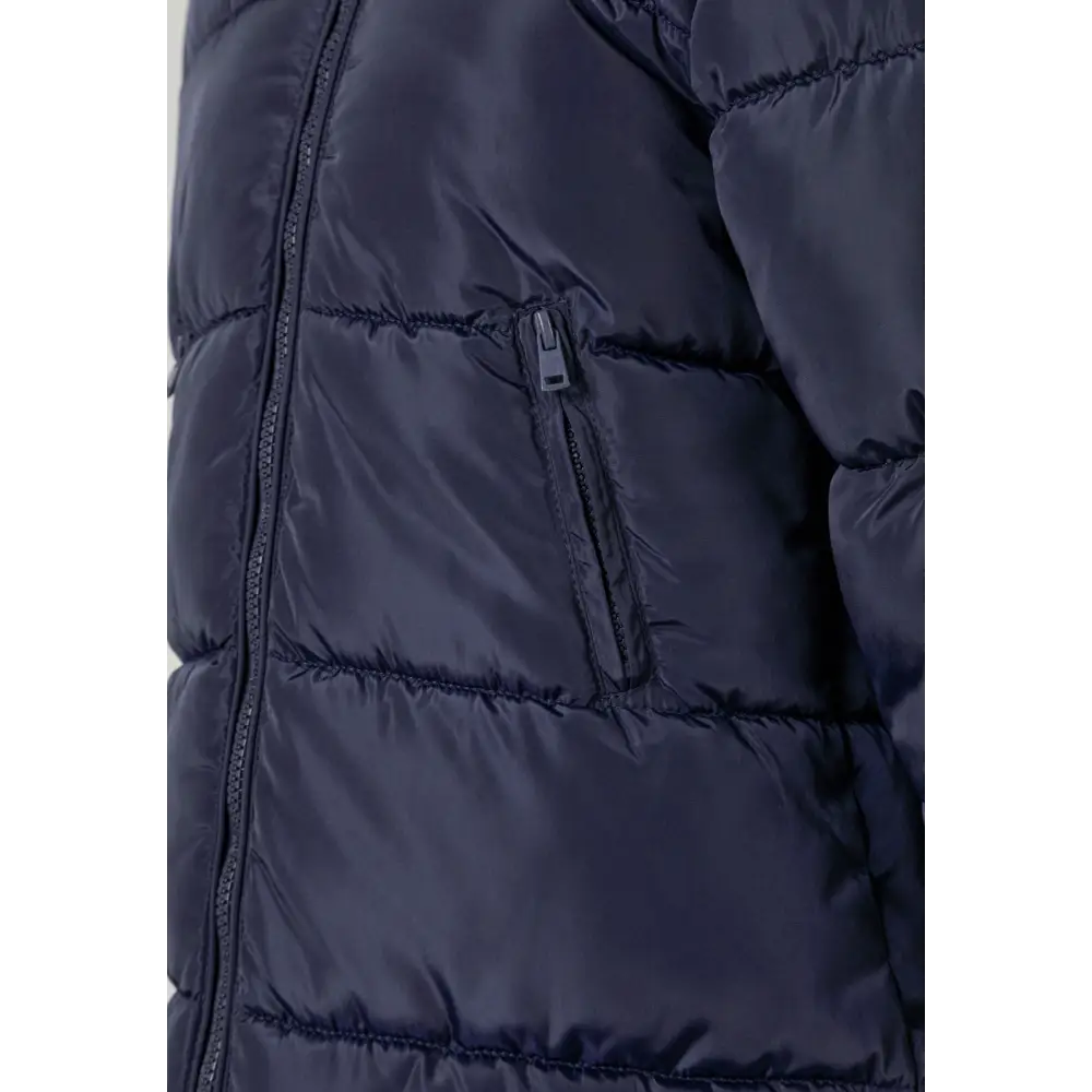 Close-up detail of navy quilted winter coat showing zip closure, side pocket with zipper, and padded quilted texture