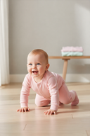 Smiling baby girl in a pink romper crawling on a light wooden floor in a bright minimalist nursery