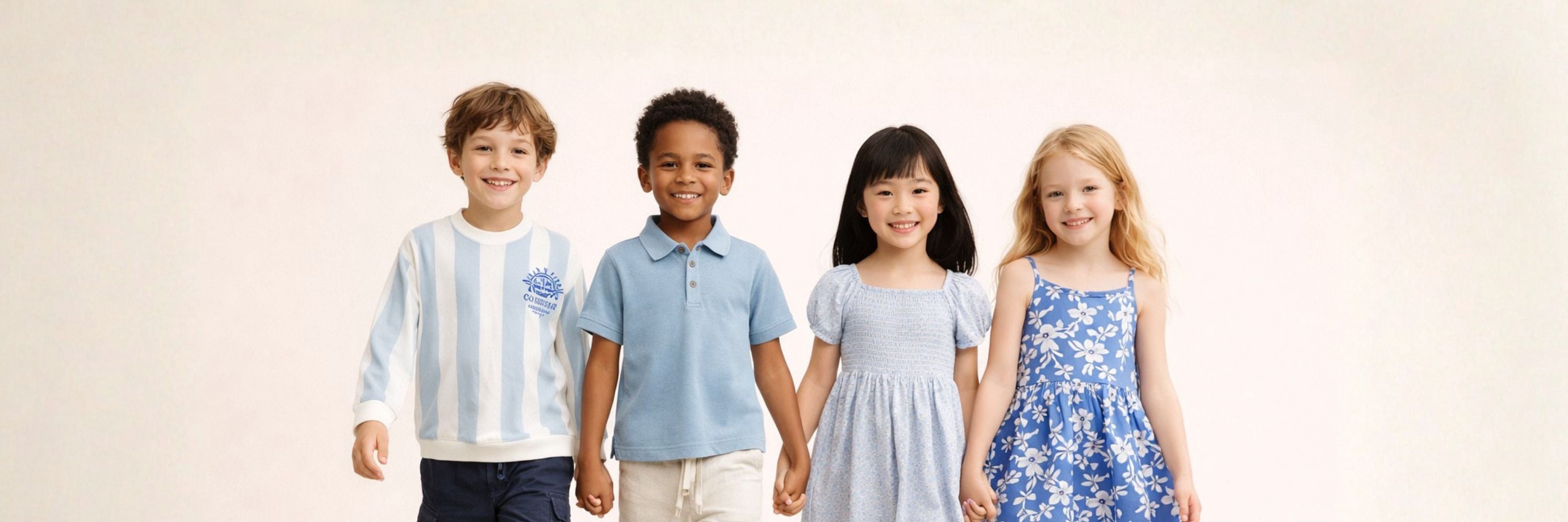 Four smiling children standing side by side in blue-toned outfits. Two boys wear a striped top and polo with shorts, while two girls wear light blue dresses, one plain and one floral.