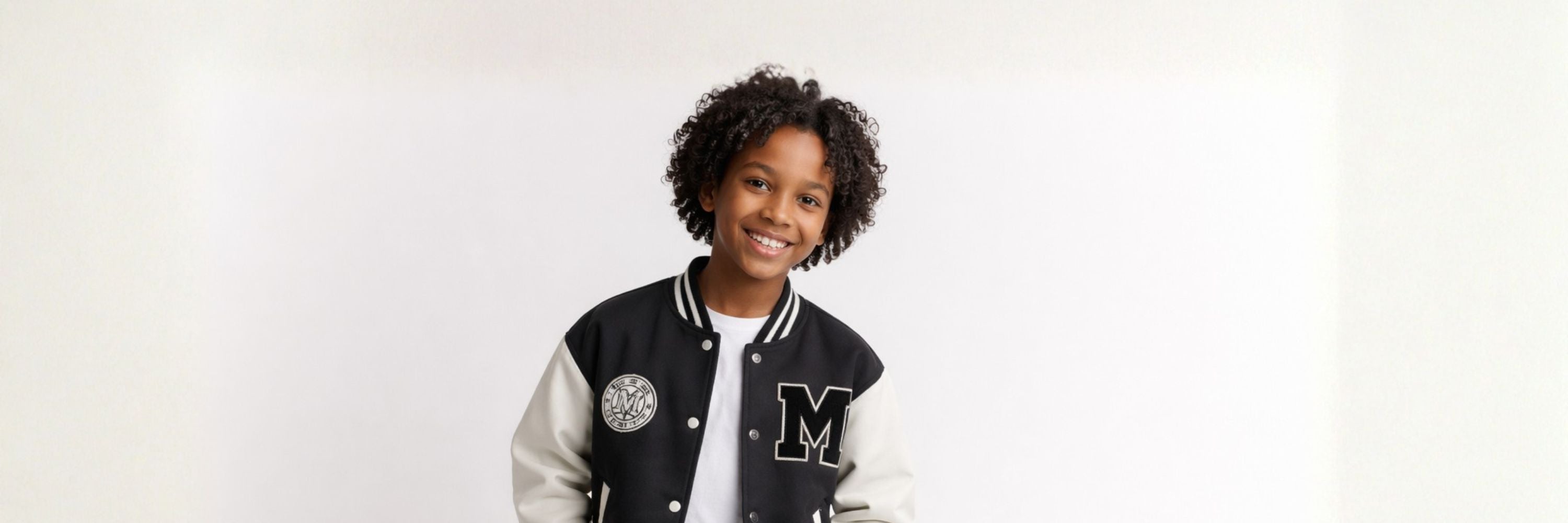 Smiling boy in a classic varsity jacket stands against a clean background, combining sporty style with a modern, casual look.
