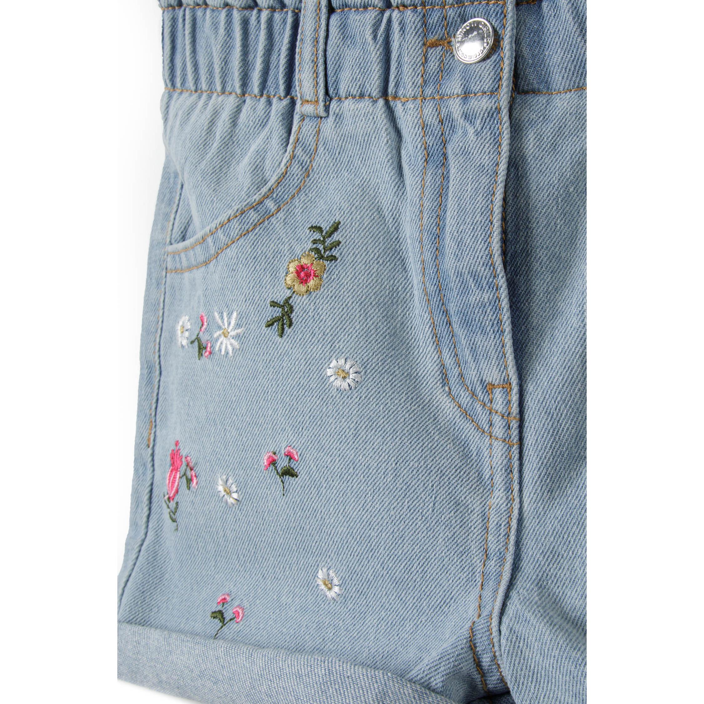 Close-up detail of floral embroidery on light blue denim showing colorful flowers, leaves and decorative stitching on white background