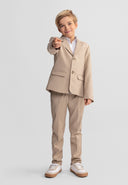 Young boy wearing a stone-colored tailored formal blazer and trousers with a confident smile and pointing gesture