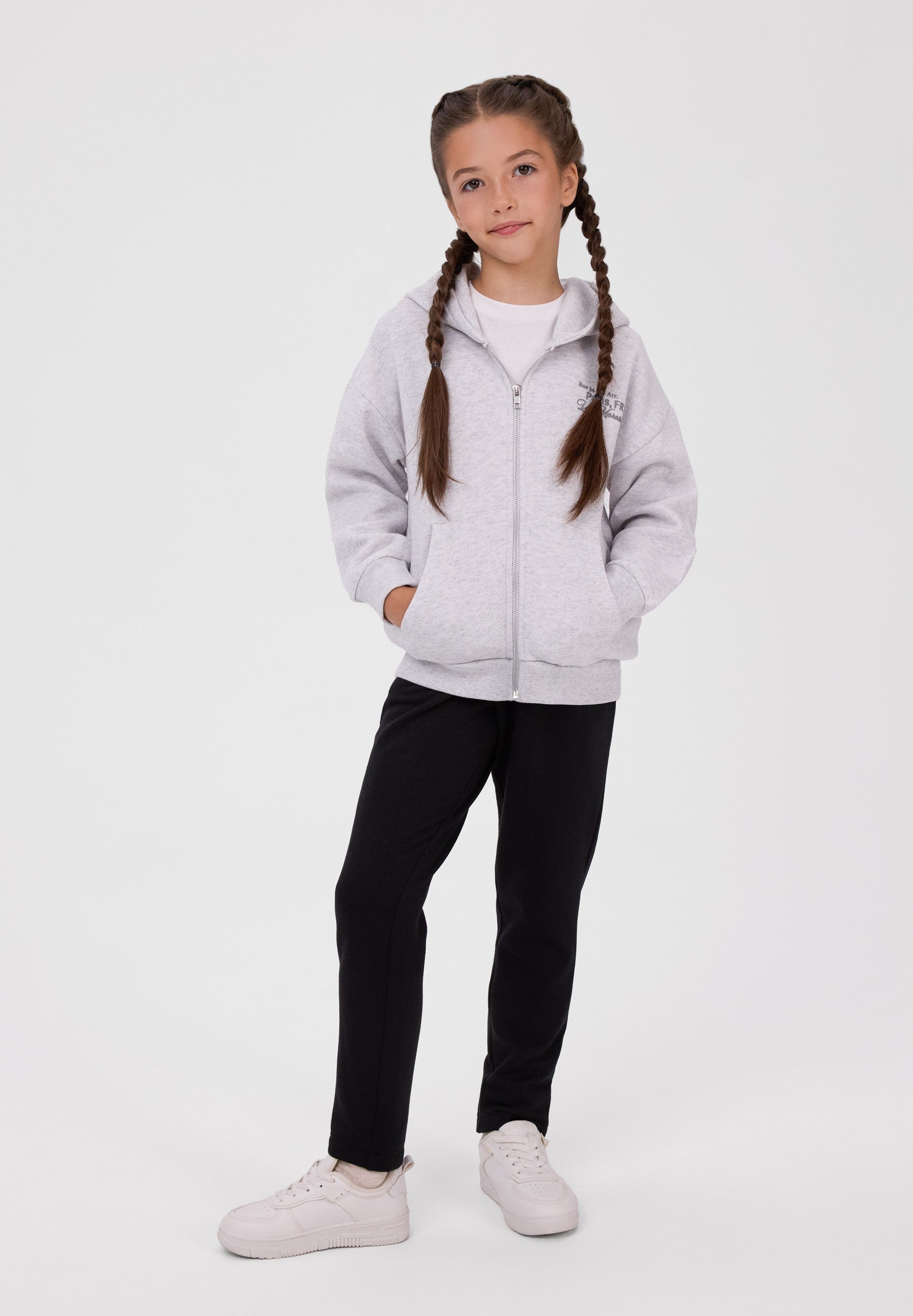 A girl wearing a gray hooded sweatshirt and black sweatpants.