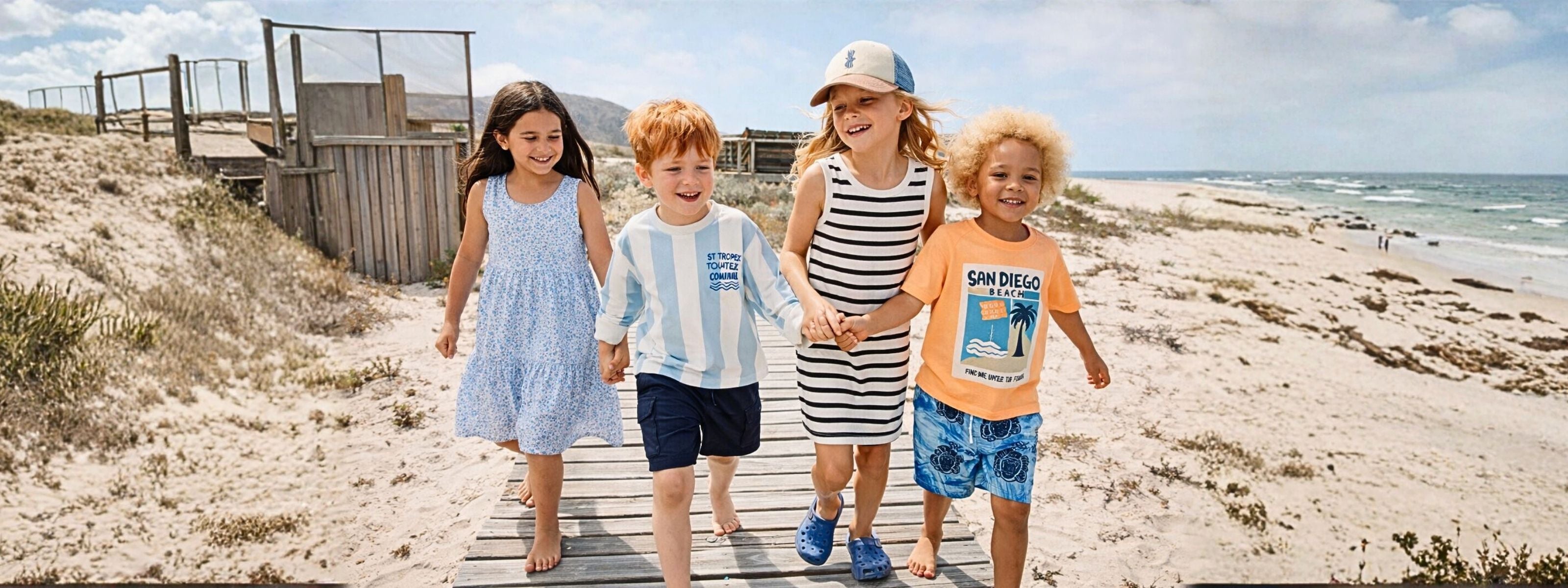 Four children walking on a wooden boardwalk at the beach.