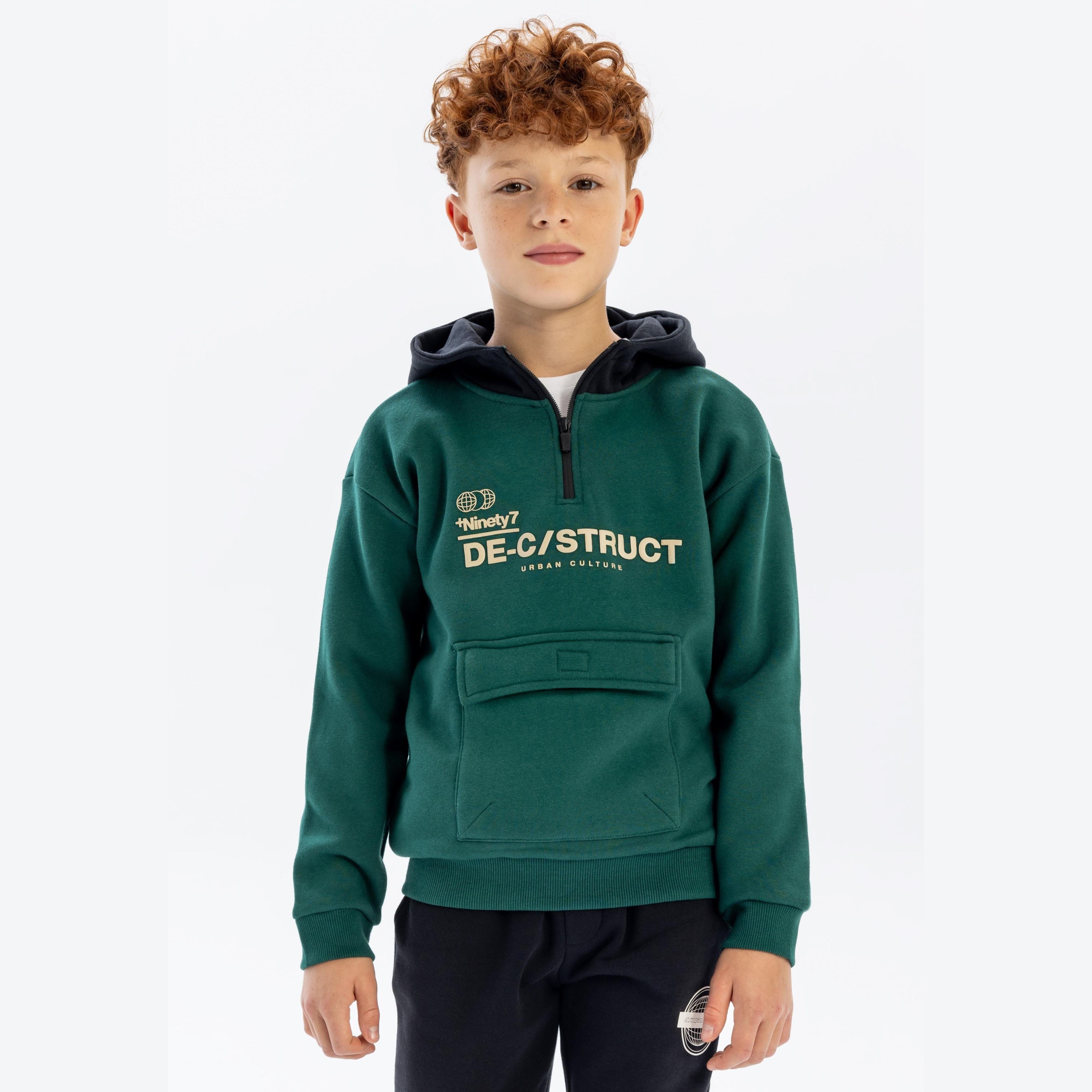 Boy wearing dark green half-zip hoodie with black contrasting hood and DE-CONSTRUCT urban print on chest, standing against white background