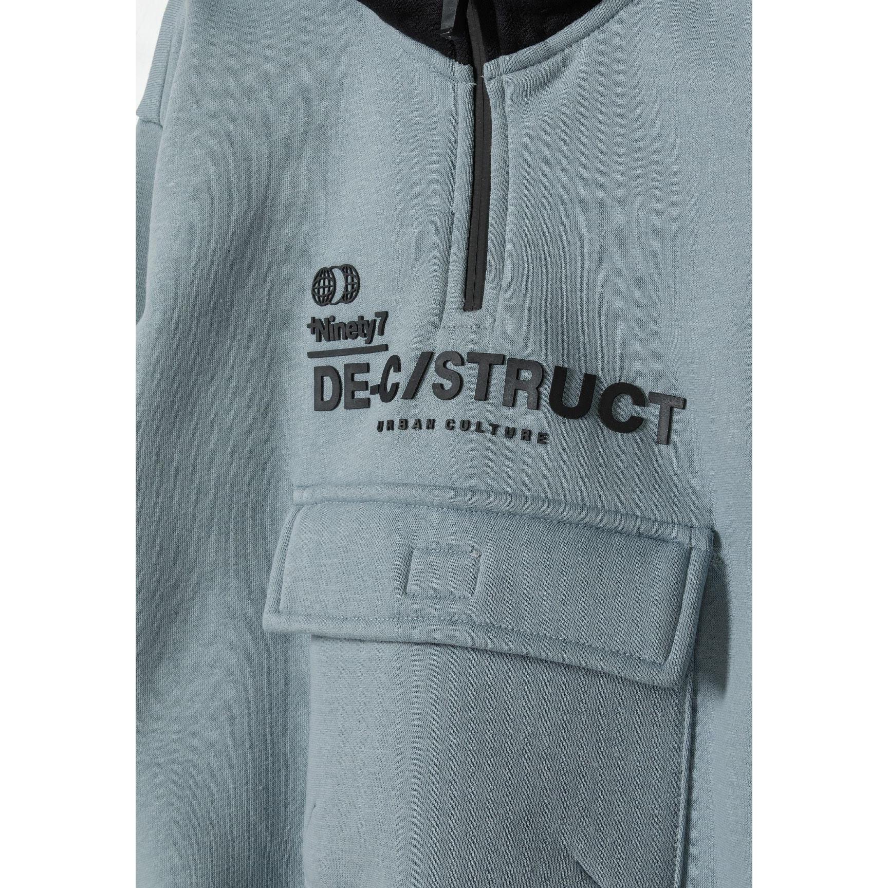 Close-up detail of blue hoodie showing Deconstruct urban culture print, front pocket, and half-zip with black trim