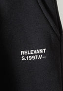 Black joggers for boys featuring a graphic print with 'RELEVANT S.1997' text. Slim fit design for ages 2-14 years.