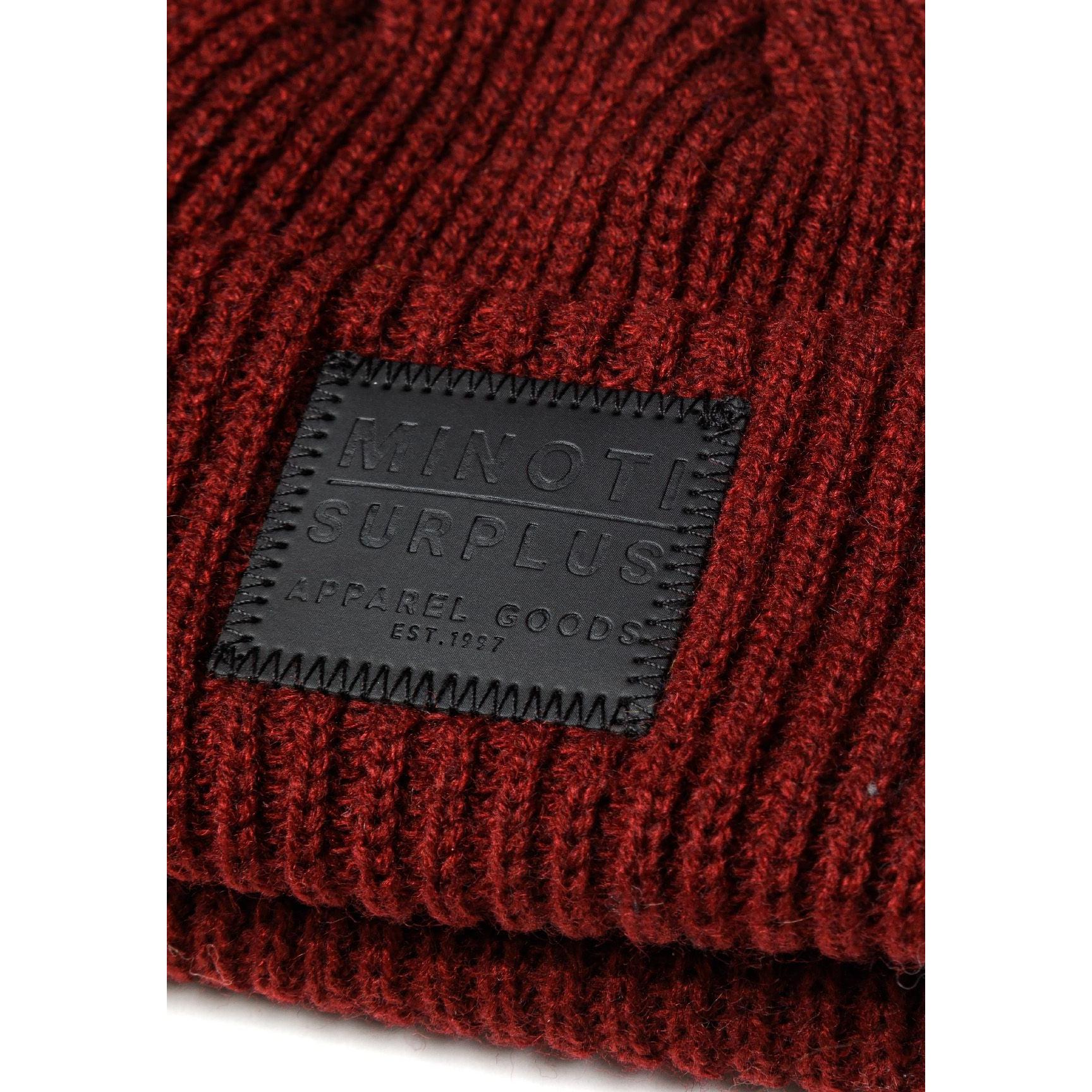 Close-up detail of burgundy ribbed knit beanie showing the embossed dark grey Minoti Surplus patch with Apparel Goods Est. 1967 text and decorative stitching around edges