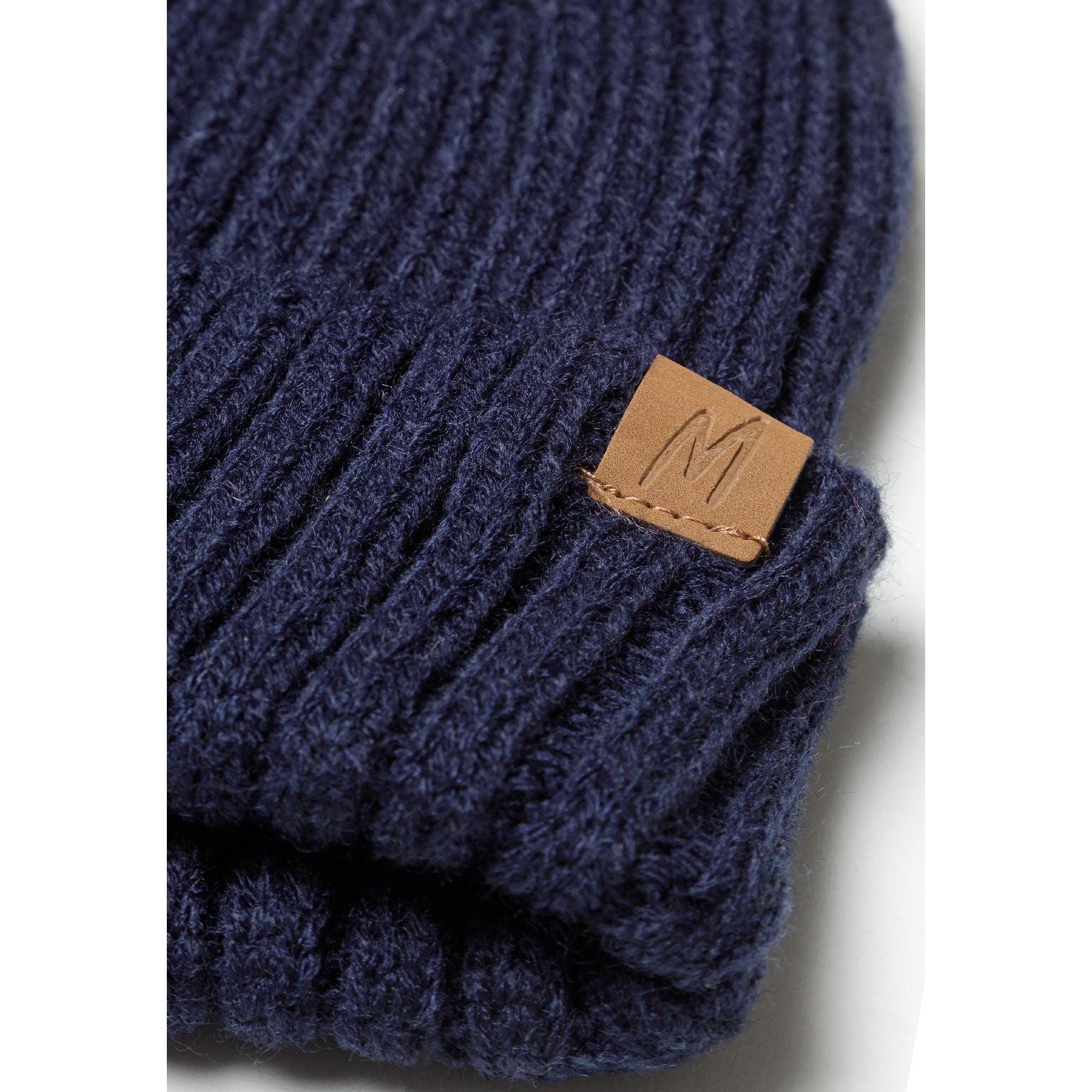 Close-up detail of navy ribbed beanie showing brown leather Minoti patch branding