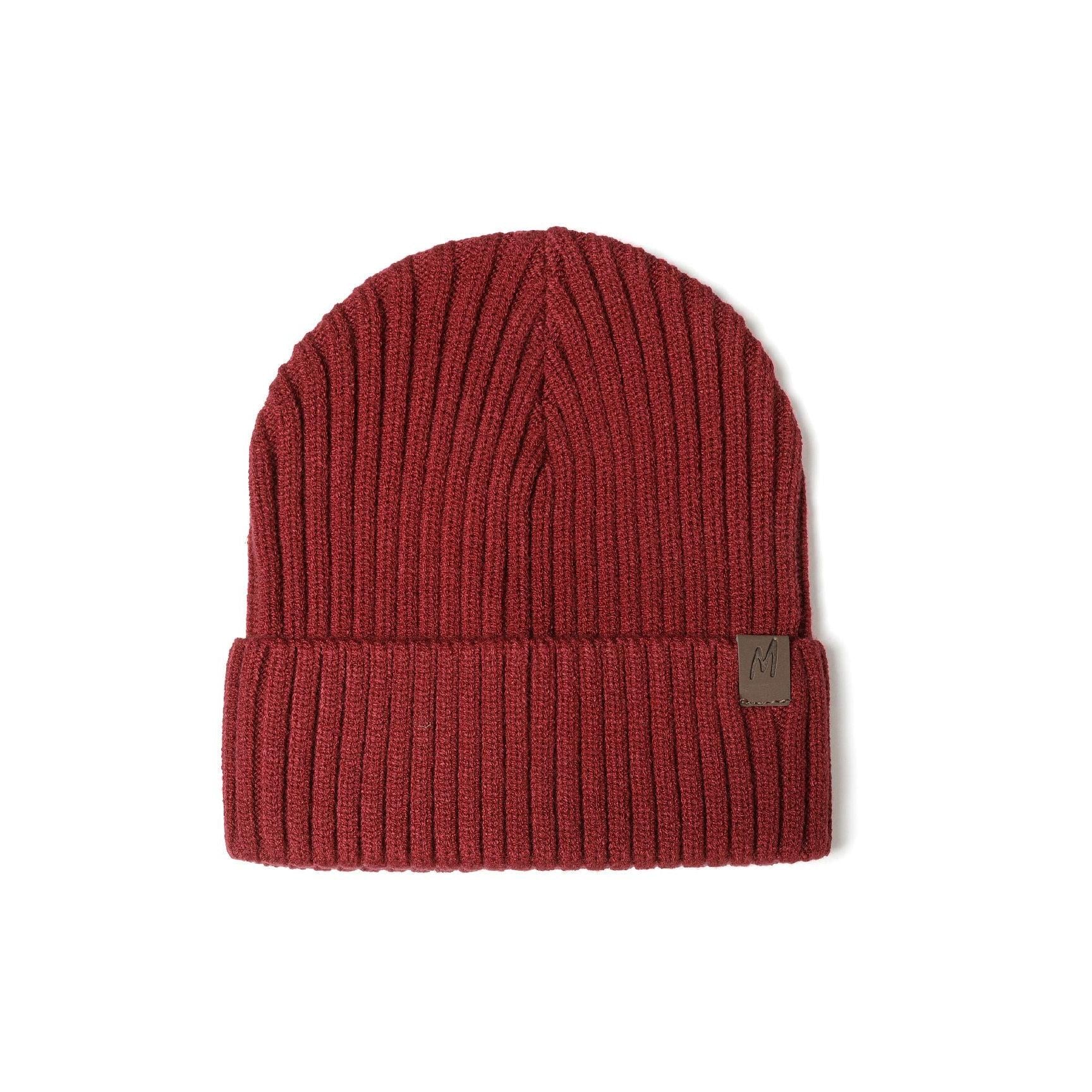 Detailed close-up of burgundy red ribbed knit beanie cuff showing brown leather-look square tab with embossed M logo against textured knit fabric