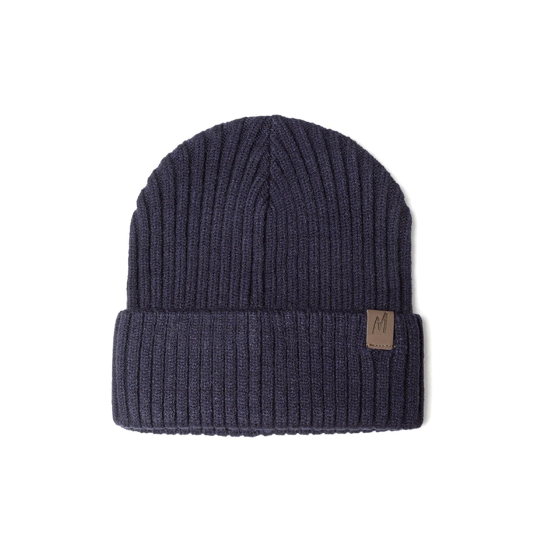 Close-up front view of navy blue ribbed knit beanie on white background showing detailed rib texture and brown leather-look tab with M logo