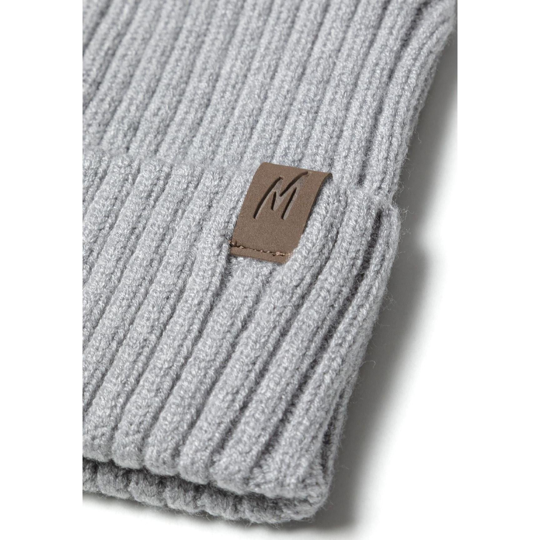 Detailed close-up of burgundy red ribbed knit beanie cuff showing brown leather-look square tab with embossed M logo against textured knit fabric