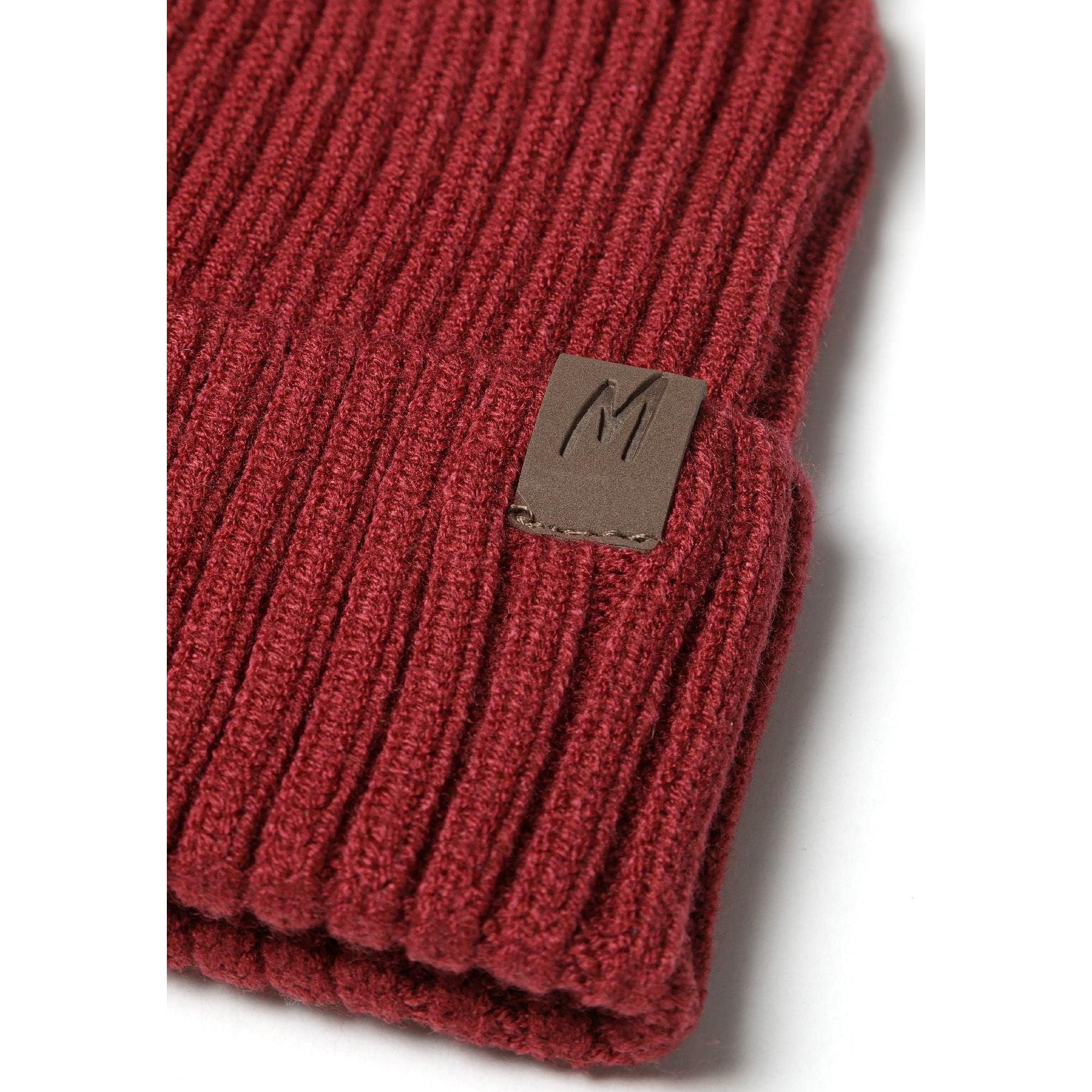 Detailed close-up of burgundy red ribbed knit beanie cuff showing brown leather-look square tab with embossed M logo against textured knit fabric