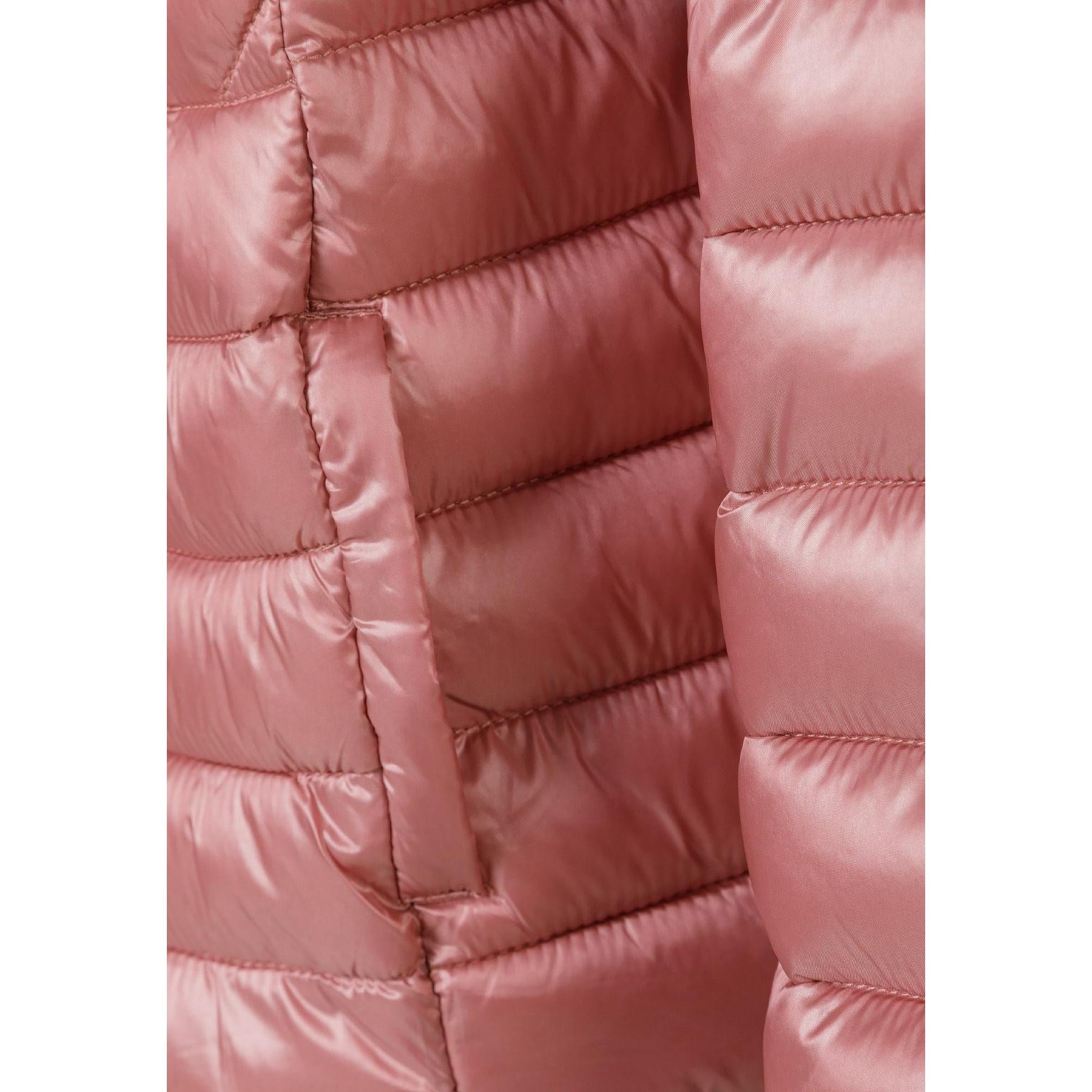 Close-up detail of copper quilted jacket sleeve showing circular embroidered patch with heart design and text